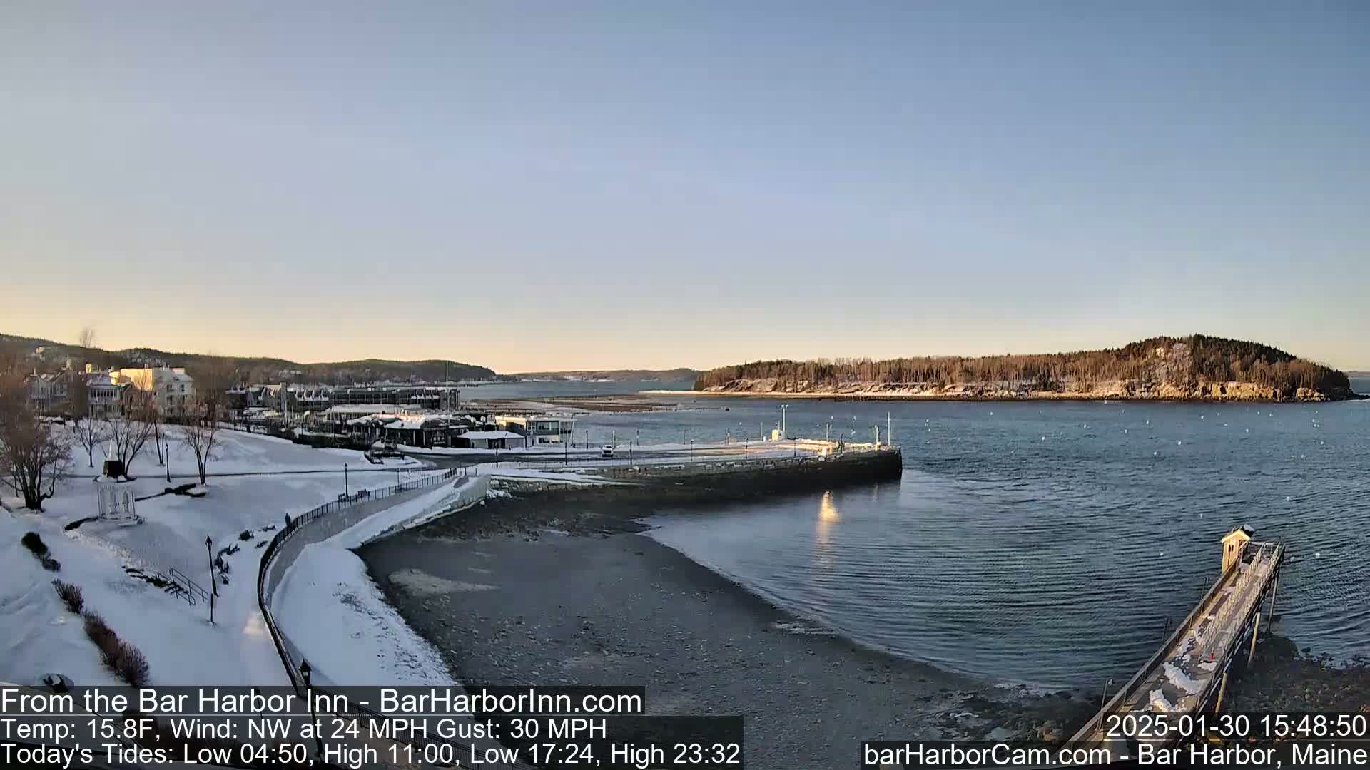 A snow-covered waterfront town and harbor are visible on a partly sunny day with a northwest wind of 24 mph and gusts up to 30 mph.