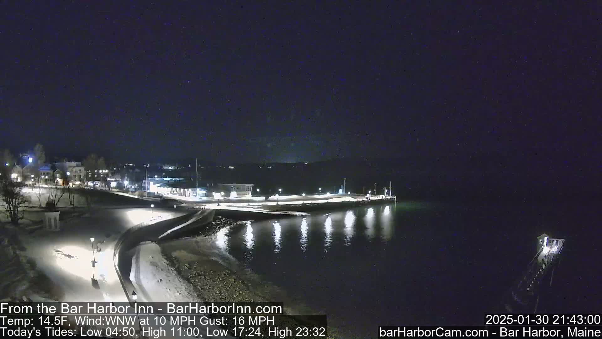A snow-covered waterfront at night, with lights illuminating a town and calm water reflecting the lights.