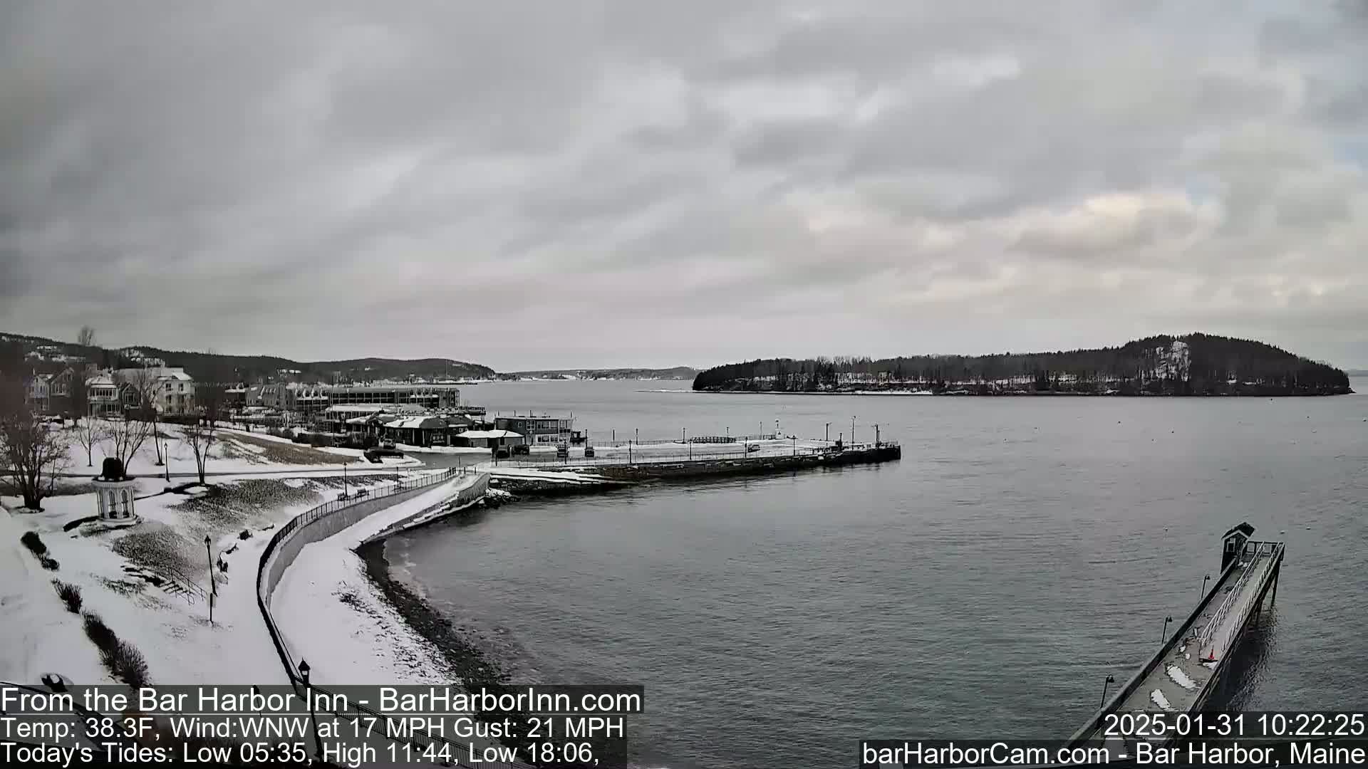 A snow-dusted waterfront town overlooks a calm bay under a cloudy sky.