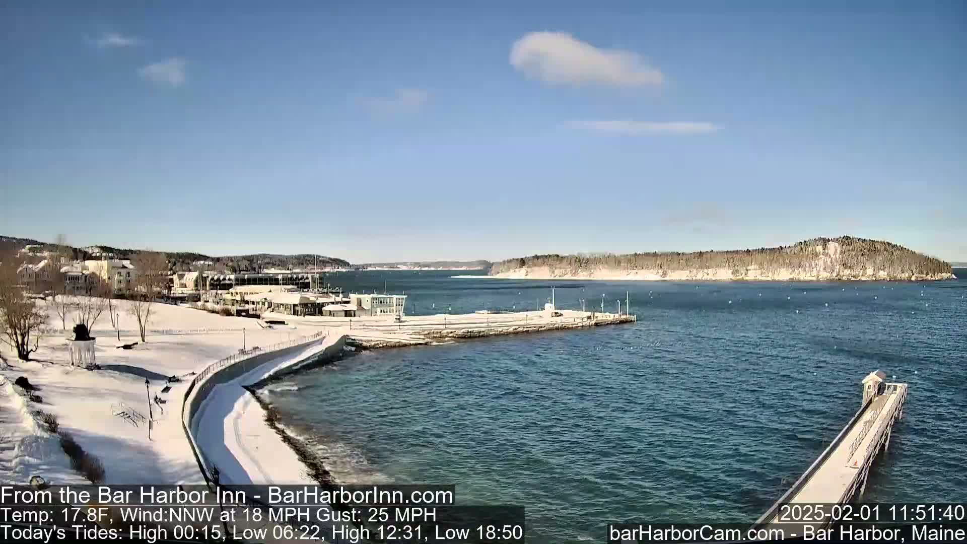 A snow-covered waterfront scene with a calm harbor, under a mostly clear, bright sky.