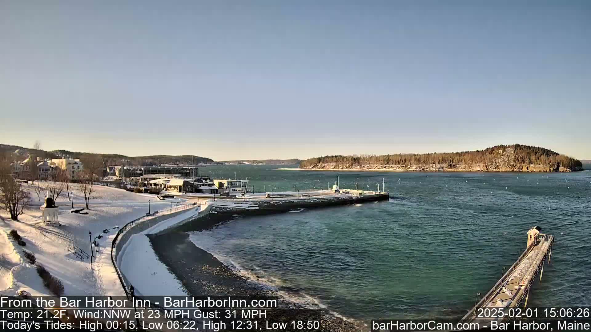 A snow-covered waterfront town overlooks a partially frozen bay under a clear, sunny sky.