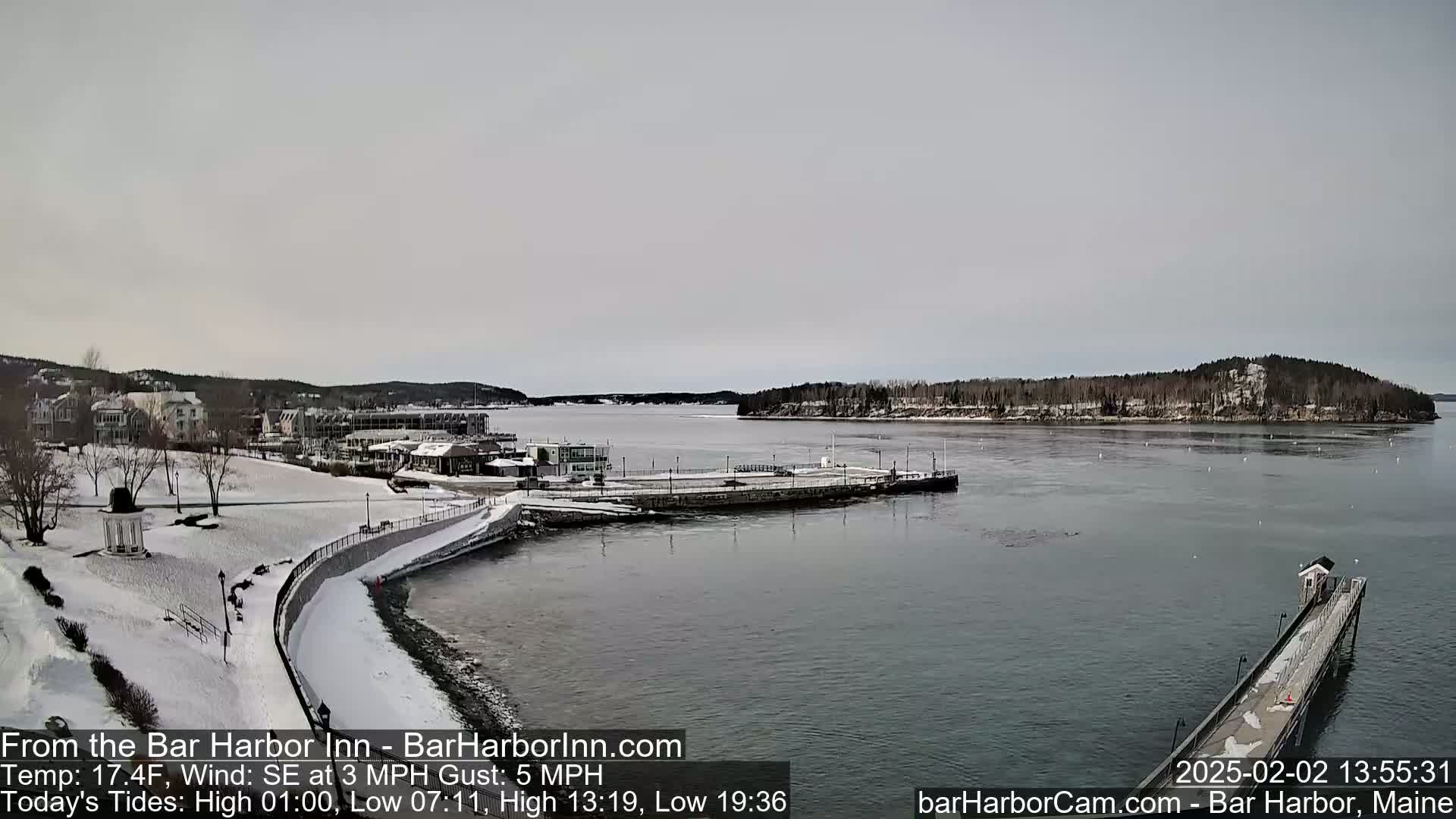 A snow-covered waterfront town is seen from across a harbor under an overcast sky.