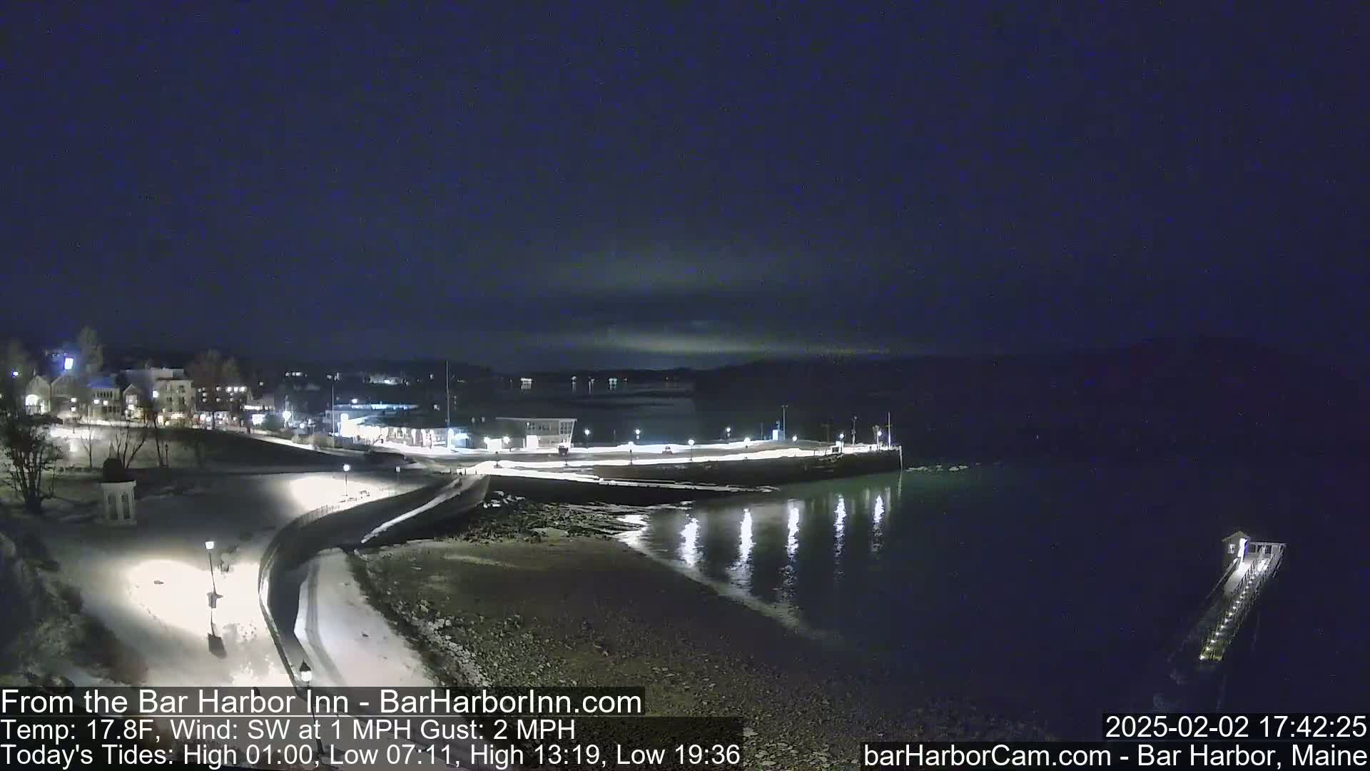 A snow-covered waterfront town at night with calm water reflecting lights, under a dark sky.