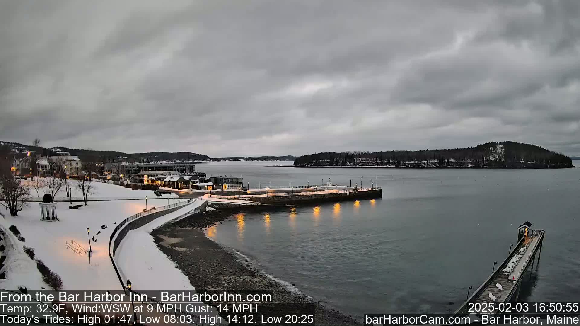 A snow-covered waterfront town overlooks a calm bay under a cloudy sky.
