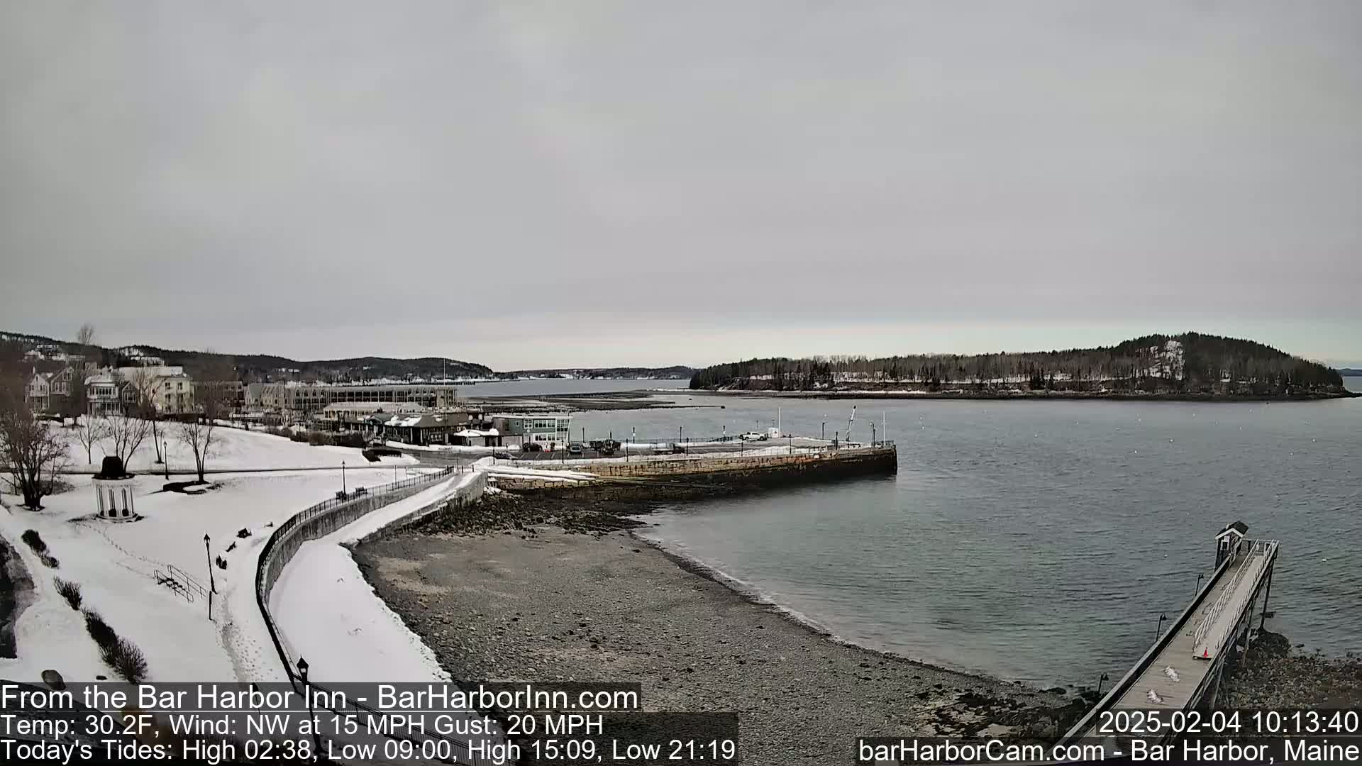 A snow-covered waterfront town with a calm, gray sky and a partially frozen harbor.