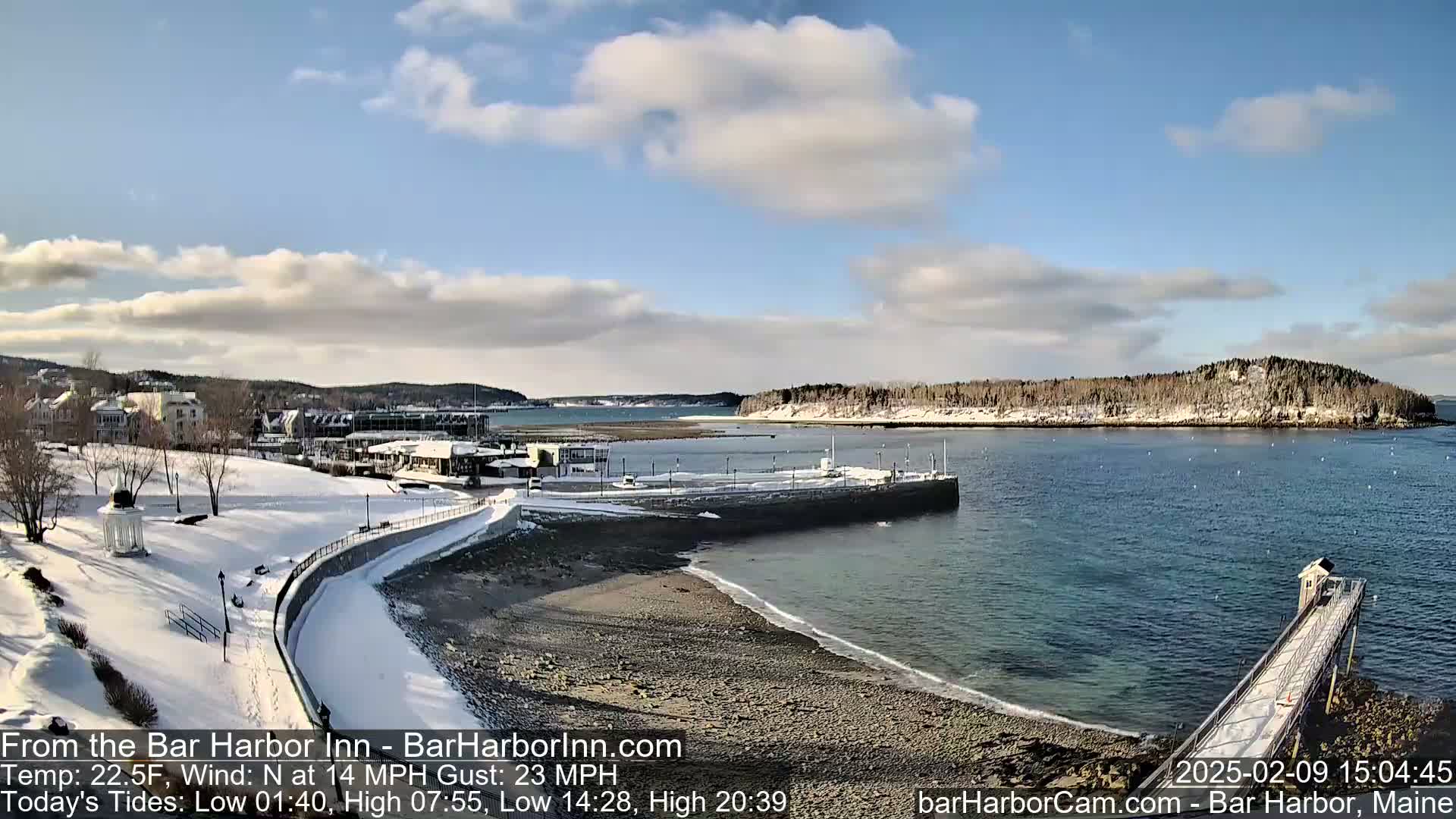 A snow-covered waterfront town with a partly cloudy sky and calm water extends to a small, snow-dusted island in the distance.