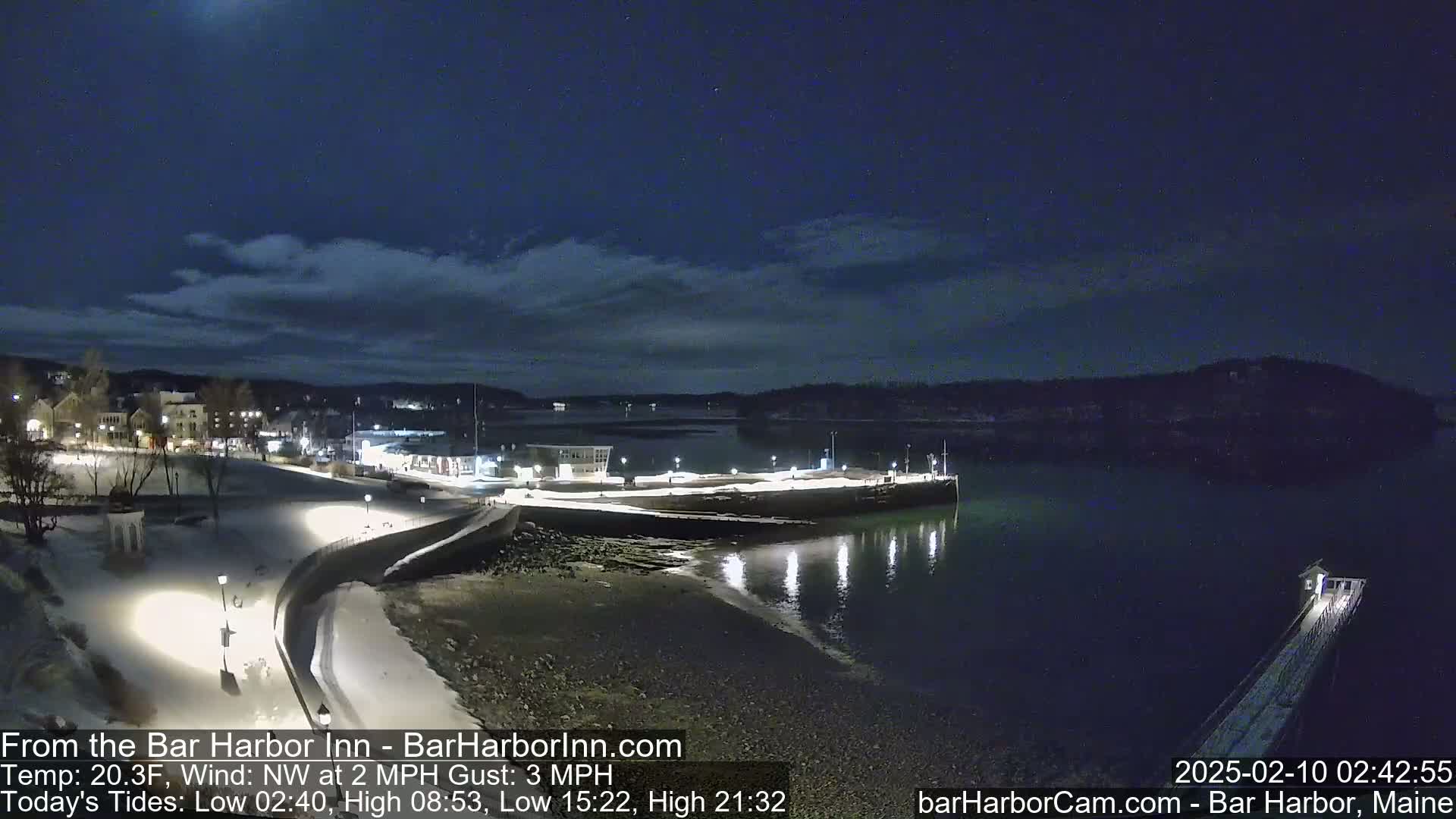 A snow-covered waterfront town at night, under a mostly clear sky, with a calm body of water reflecting the lights from the shore.