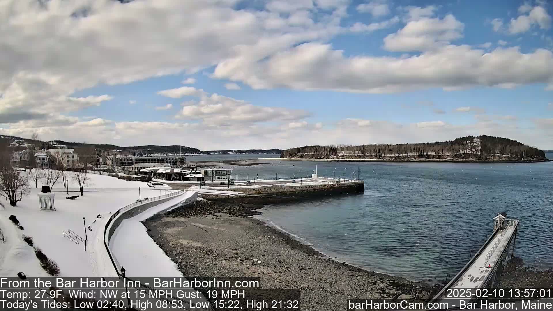 A snow-covered shoreline with a partially frozen harbor, under a partly cloudy sky.