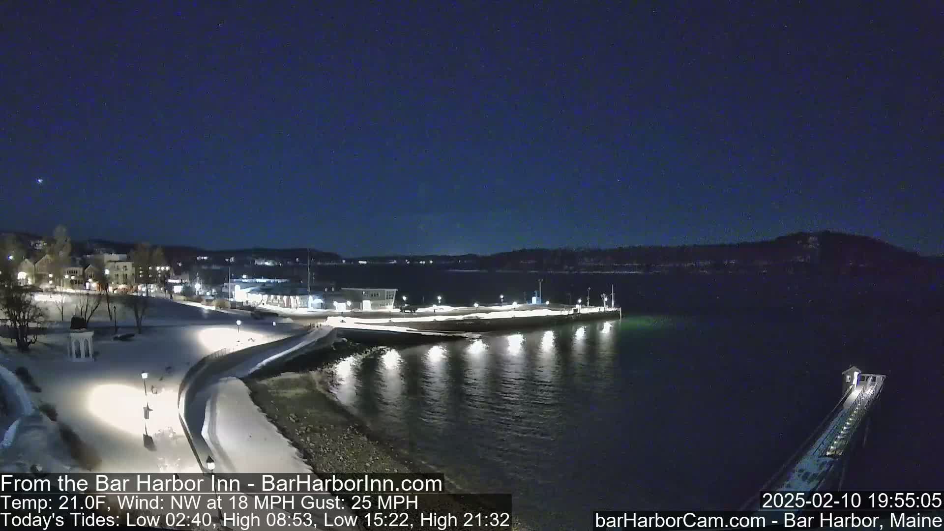 A snow-covered waterfront at night, illuminated by lights along a walkway and pier, under a clear, starry sky with a northwest wind.