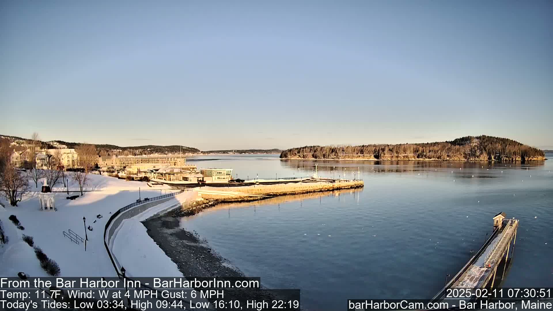 A snow-covered waterfront town overlooks a calm bay under a clear, sunny sky.