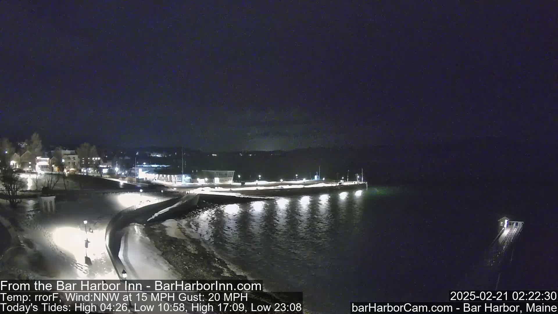 A nighttime view of a snow-covered harbor with a town in the background, under a dark sky with a northwest wind at 15 mph and gusts up to 20 mph.