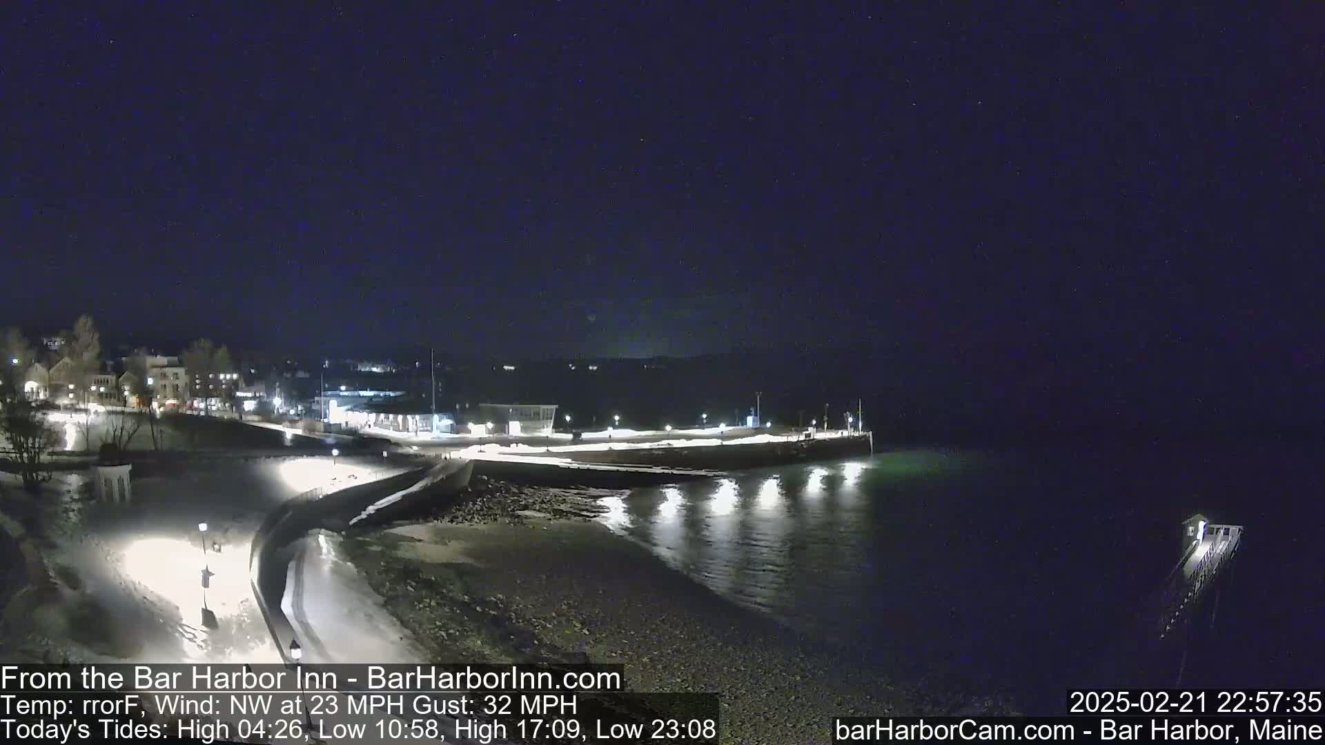 A nighttime view of a snow-covered harbor town and partially frozen coastline under a clear, dark sky with a northwest wind.