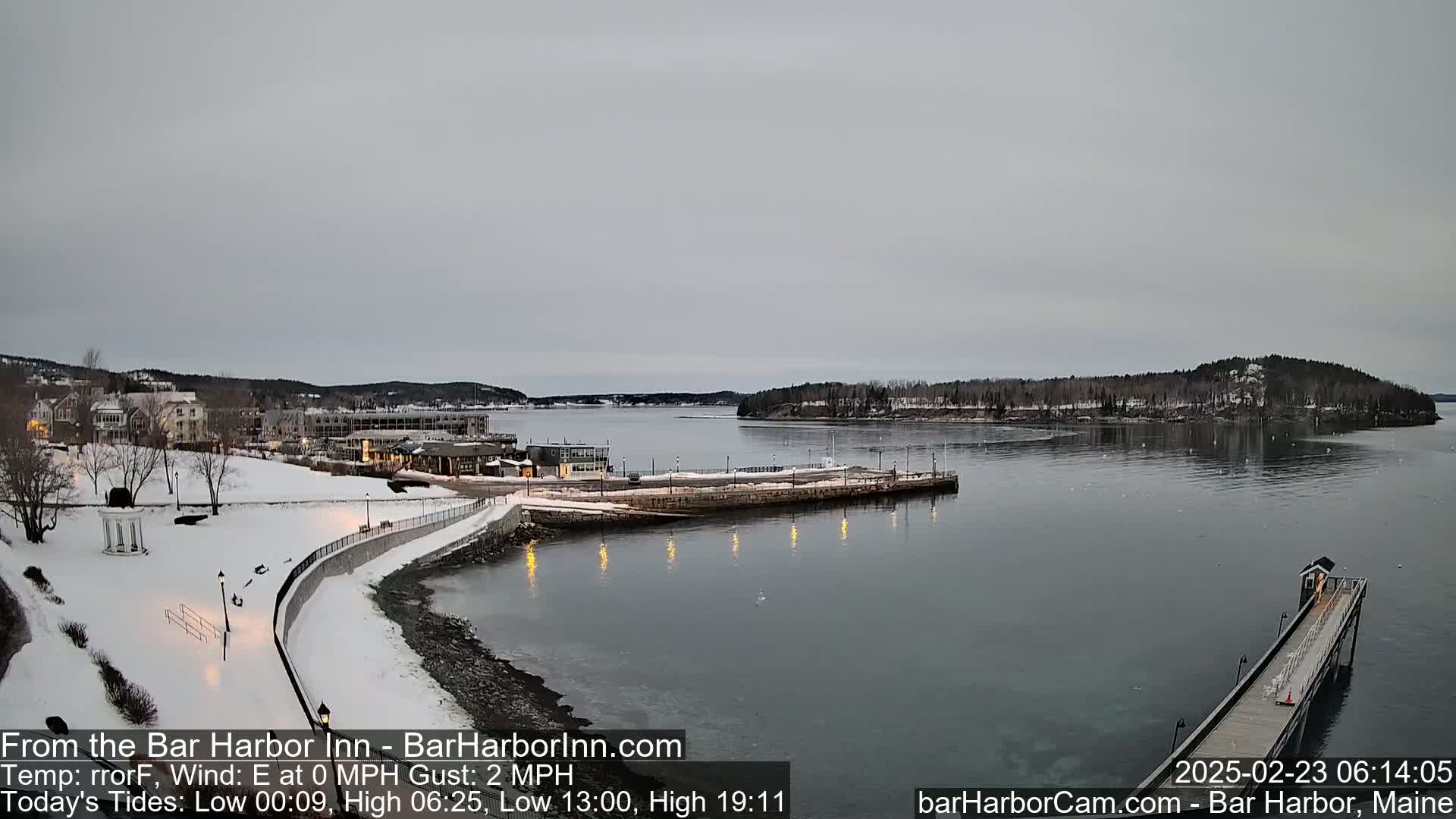 A snow-covered waterfront town with a calm harbor under an overcast sky.