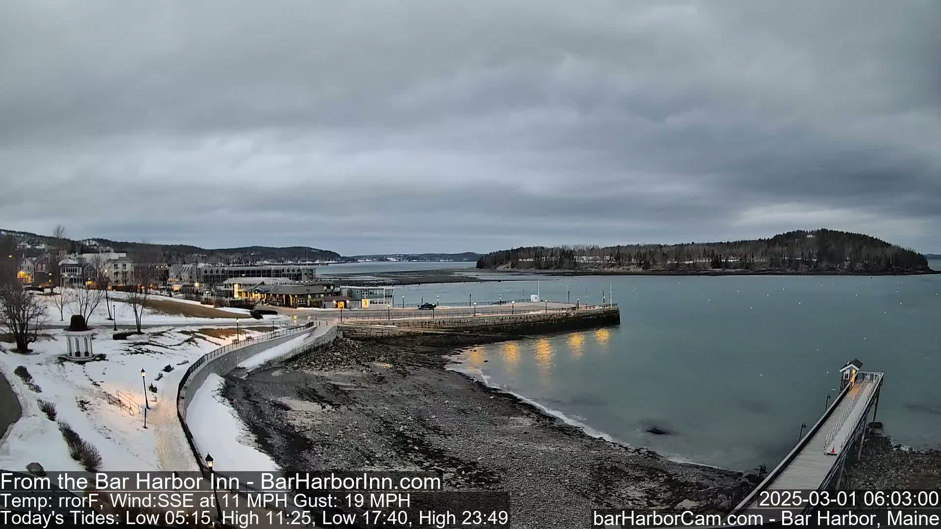 A coastal town on a partly cloudy day with snow on the ground, featuring a harbor with a long pier extending into the water.