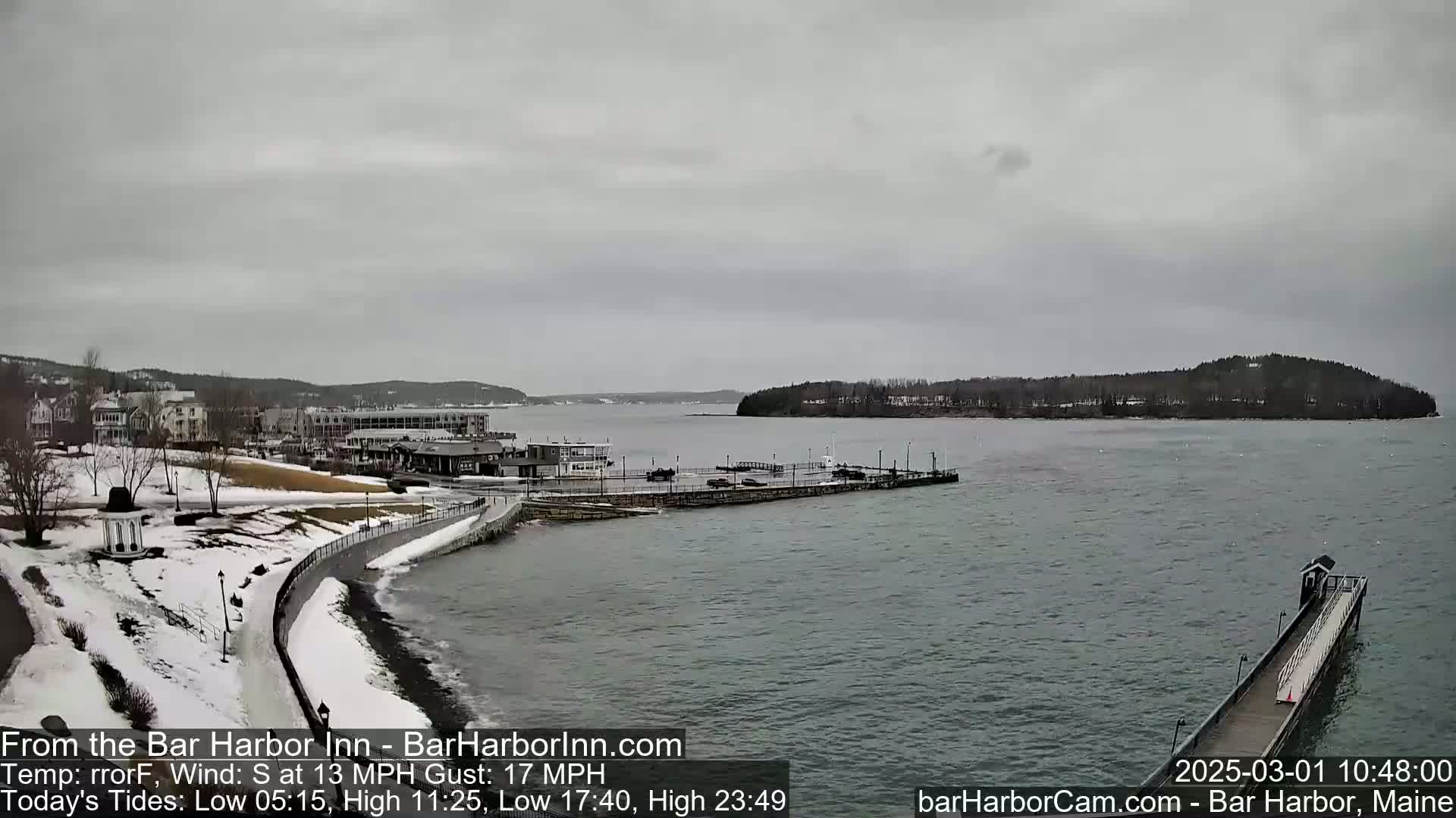 A snow-dusted coastal town overlooks a calm, gray harbor under an overcast sky.