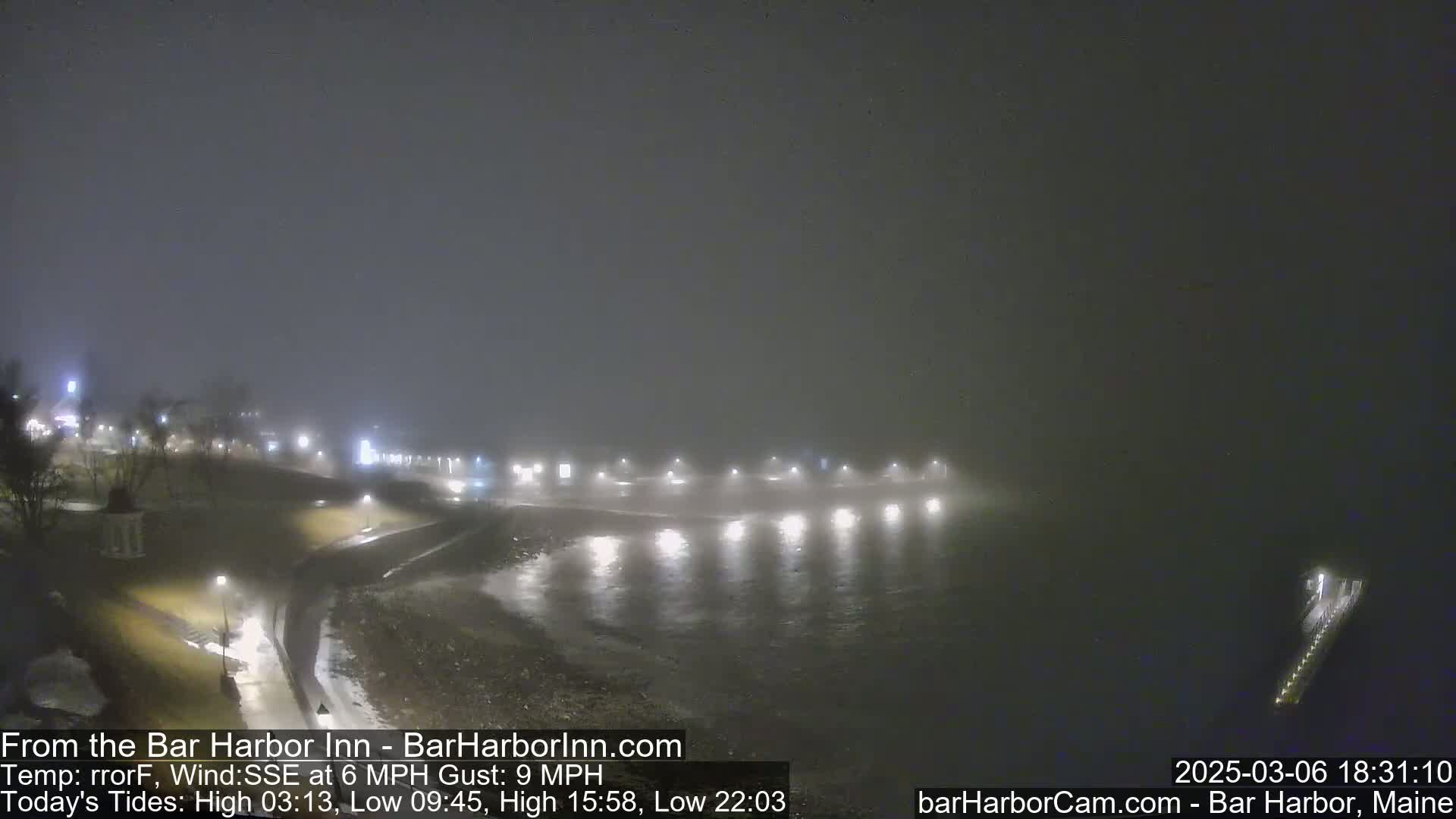 A foggy night scene shows a dark shoreline with lights along a waterfront, partially obscured by the fog, and a dark body of water.
