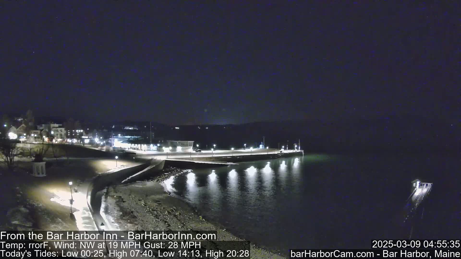 A nighttime view of a calm harbor with a town in the background under a clear, dark sky.