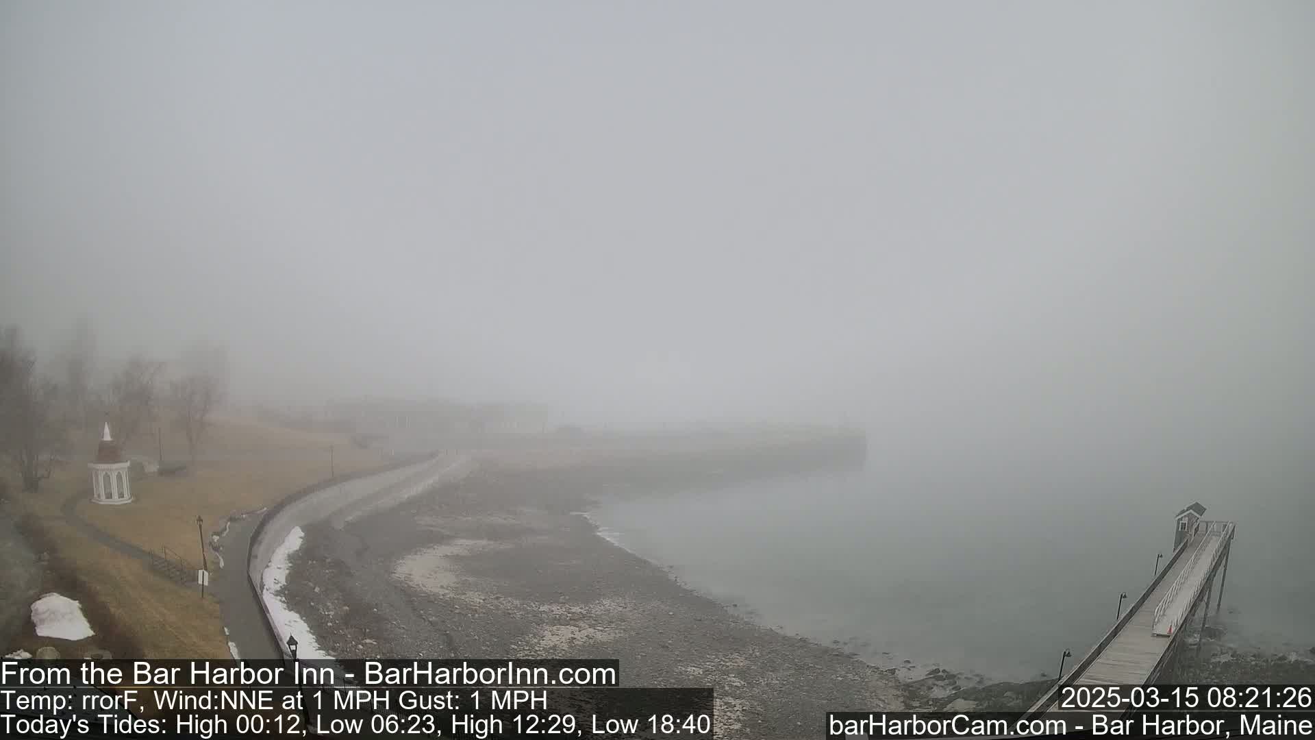 A foggy coastal scene shows a rocky shoreline, a long pier extending into the water, and a small gazebo-like structure in the distance.