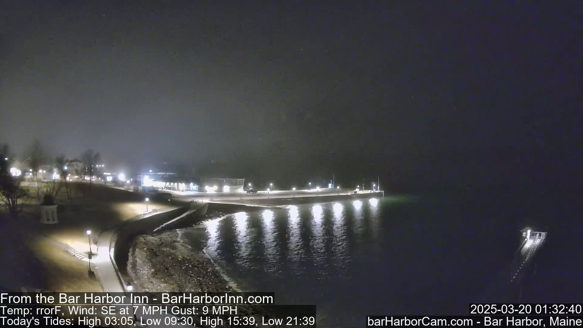 A nighttime view of a calm harbor with a shoreline featuring lights and buildings under a dark, clear sky.
