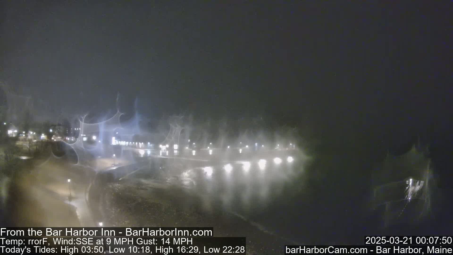 A nighttime coastal scene shows a hazy, foggy waterfront with lights reflecting on the water under a dark sky.
