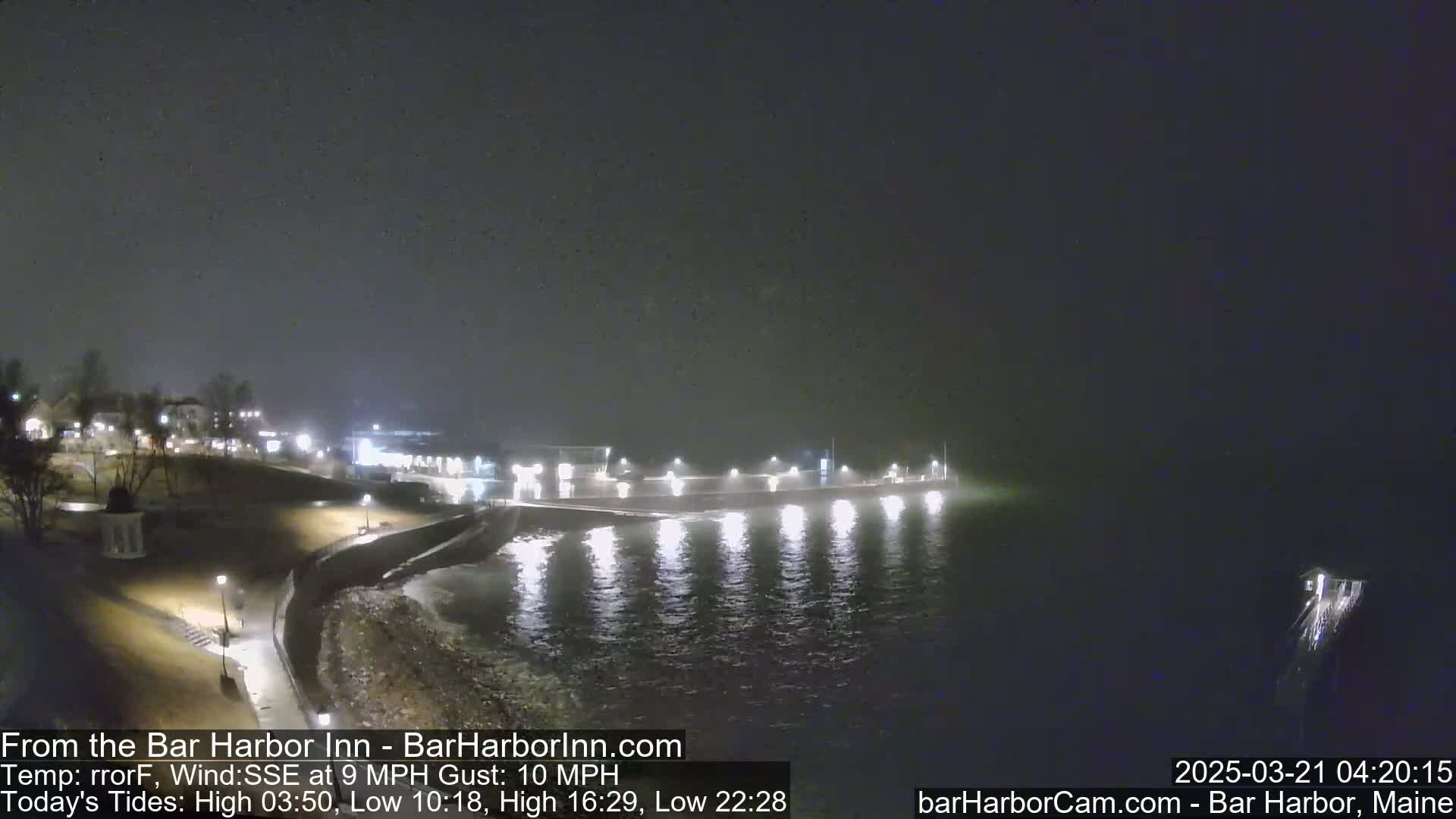 A nighttime view of a snow-covered shoreline with a lit pier extending into a dark, calm body of water.