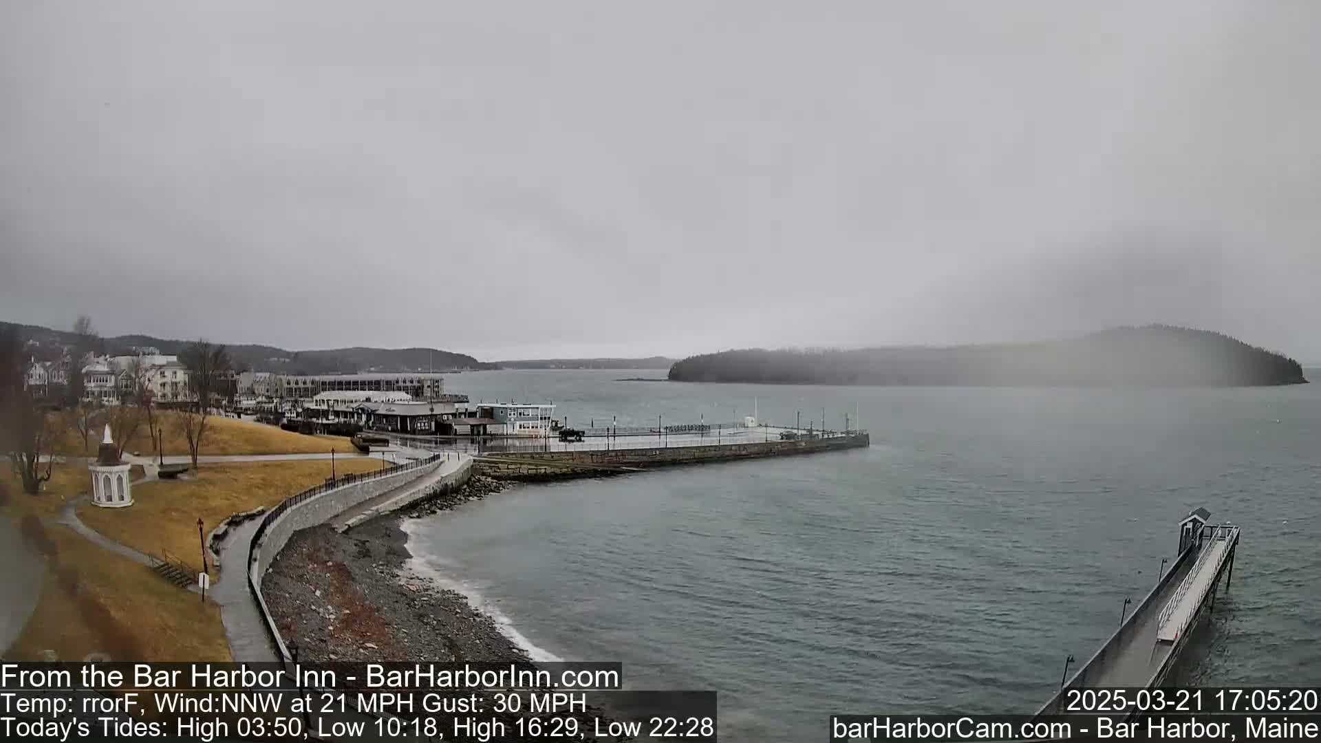 A coastal town with a pier and calm water is seen on an overcast day with a strong wind.