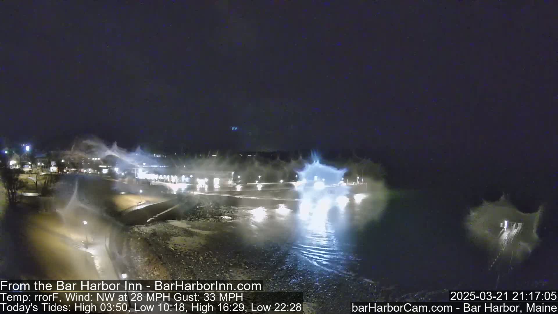 At night, under a dark sky, waves crash against a shoreline, spraying water and foam into the air in a windy scene.