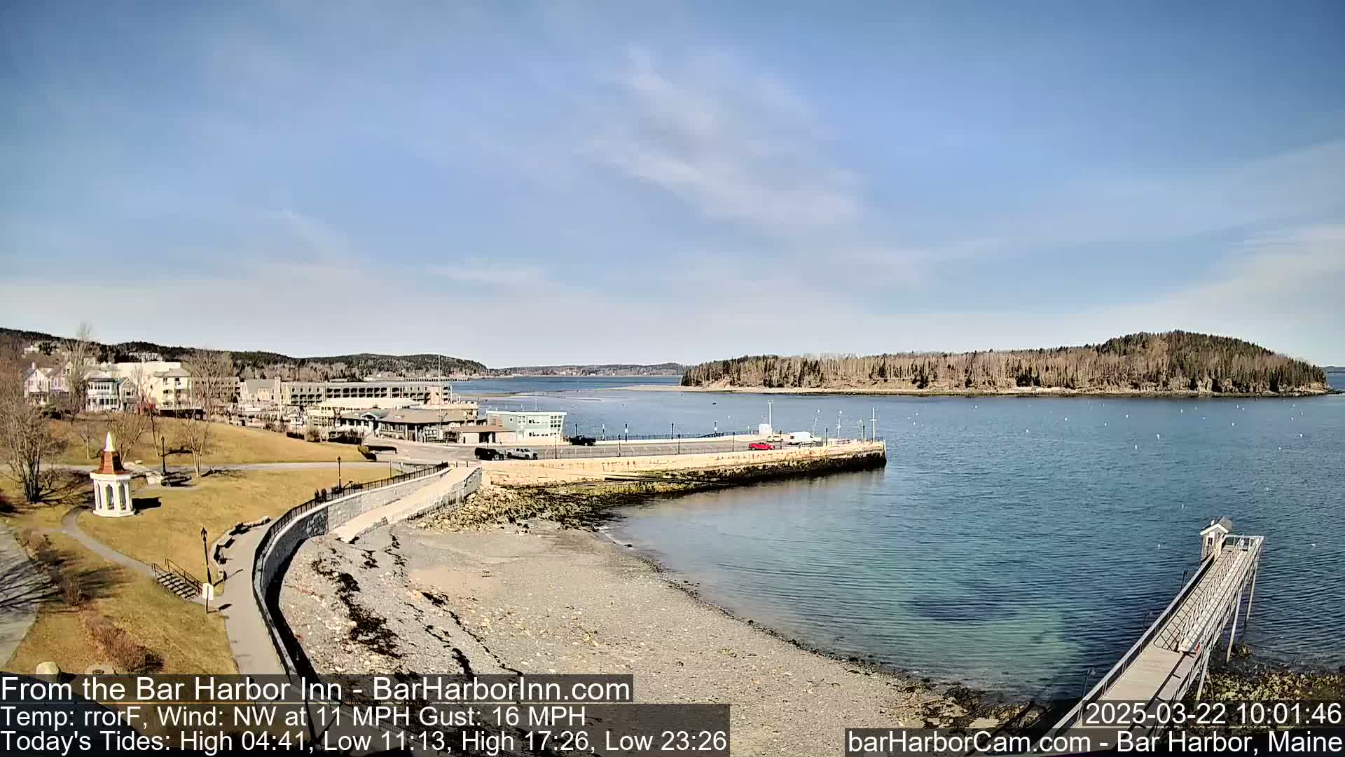 A seaside town with buildings and a grassy area sits on a calm bay under a clear, sunny sky.