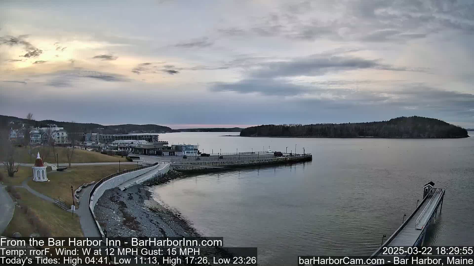 A coastal town with a harbor and a long pier is visible under a mostly cloudy sky.
