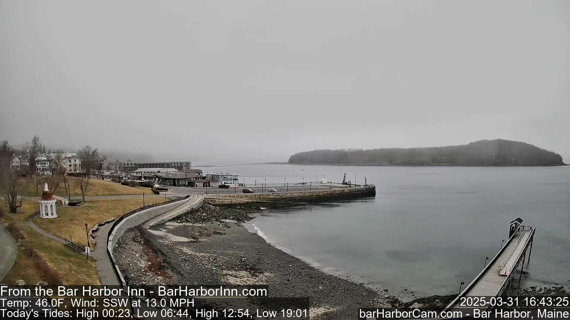 A hazy, overcast day reveals a rocky shoreline, a small town, a harbor with a pier, and an island in the distance.