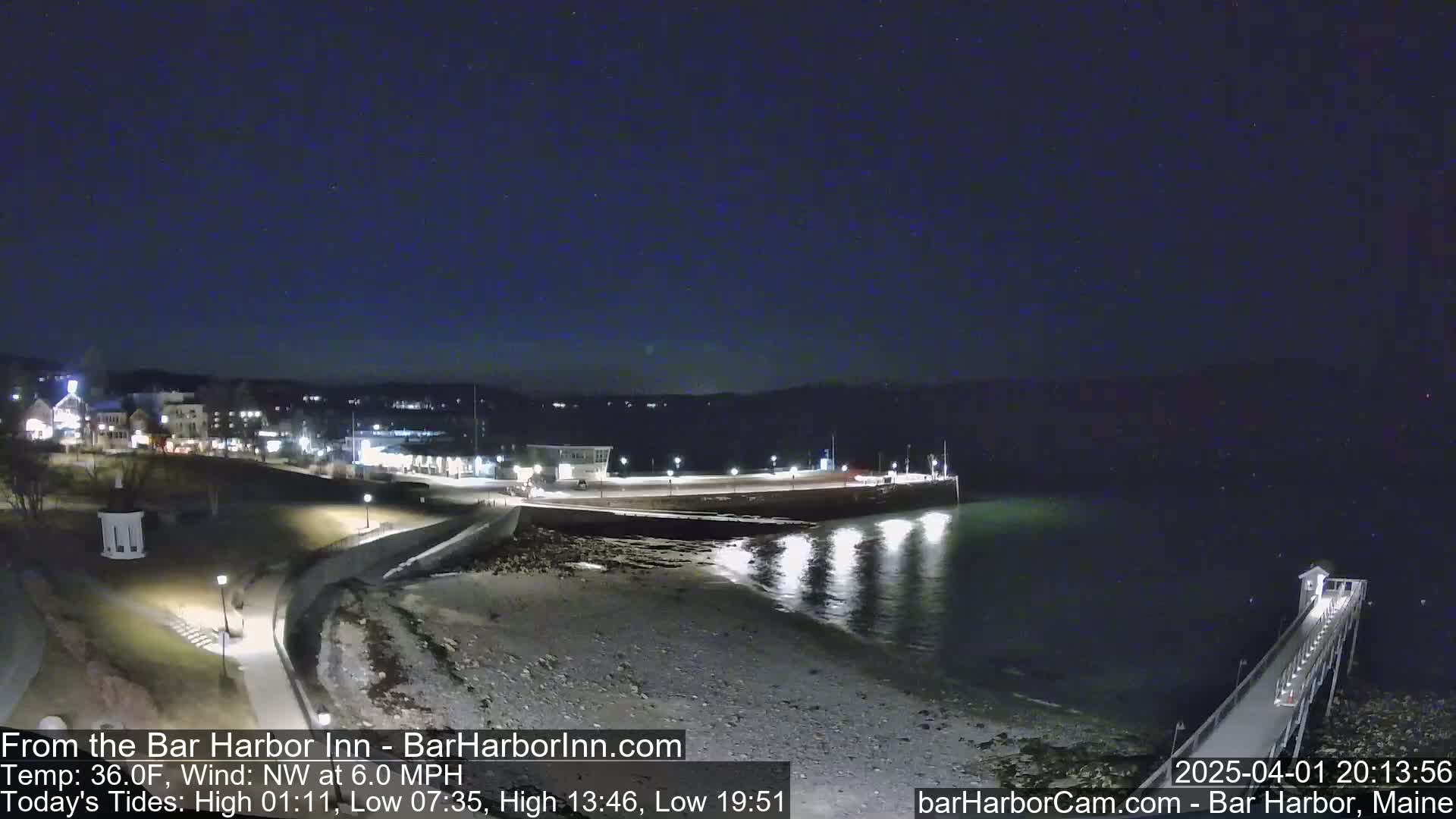 A nighttime view of a harbor with a long pier extending into calm water under a clear, dark sky.