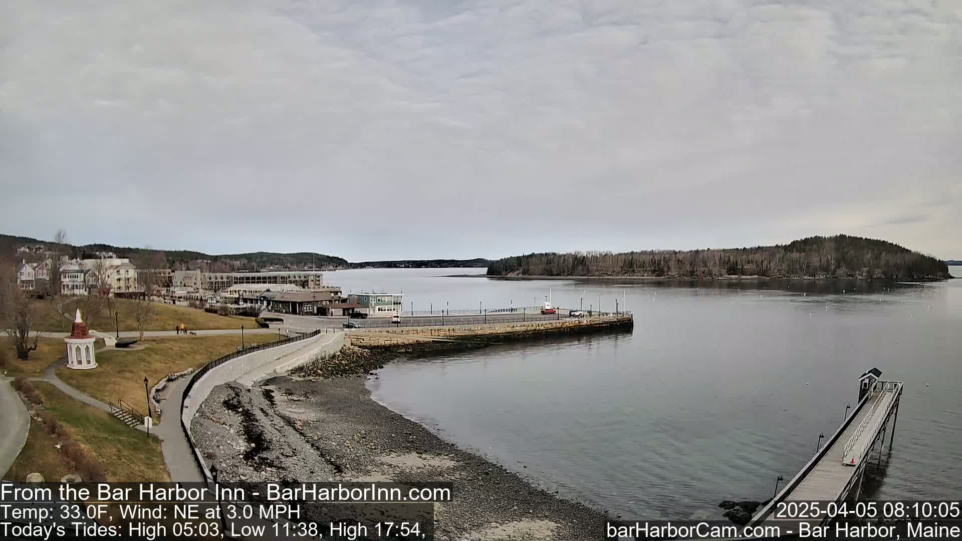 A seaside town with buildings and a long pier extends into a calm bay under an overcast sky.