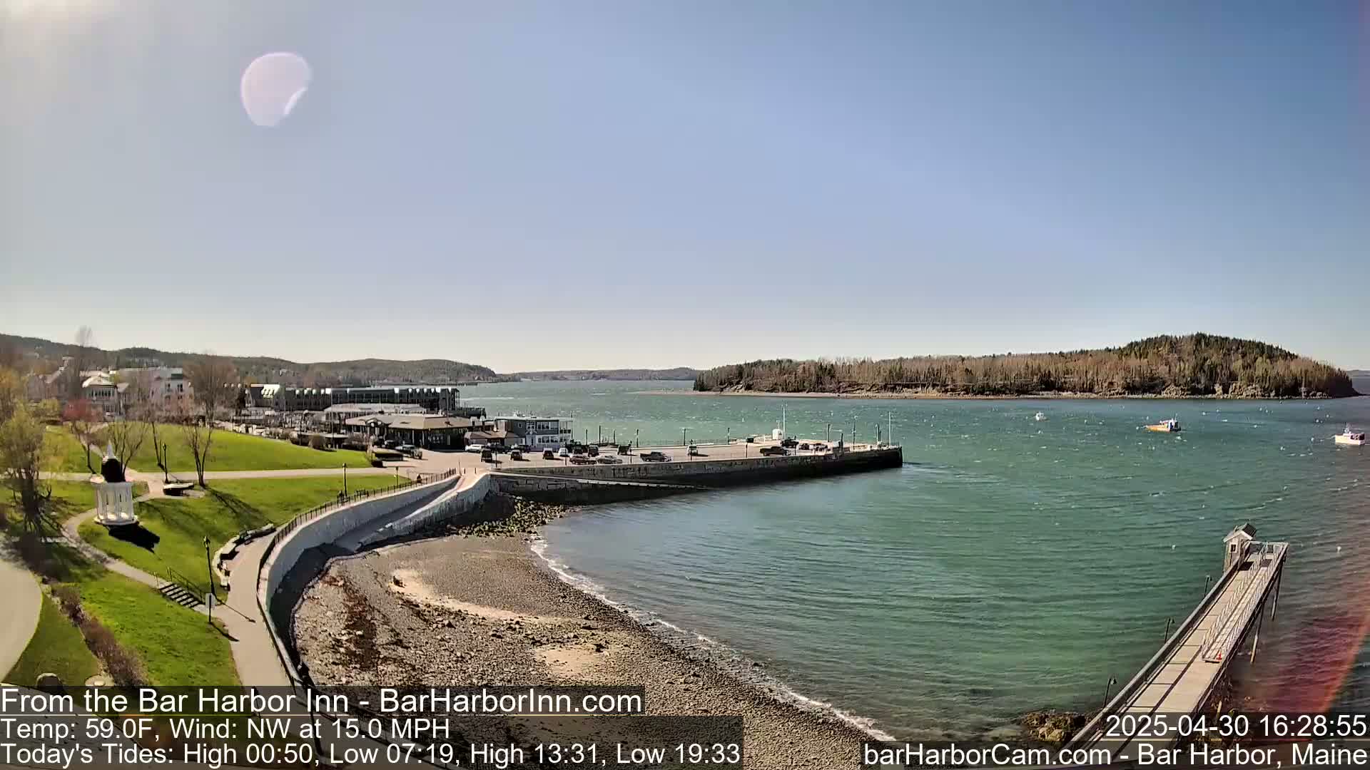 A partly sunny day shows a coastal town with a harbor, a grassy park, and several boats on the water with a northwest wind at 15 mph.