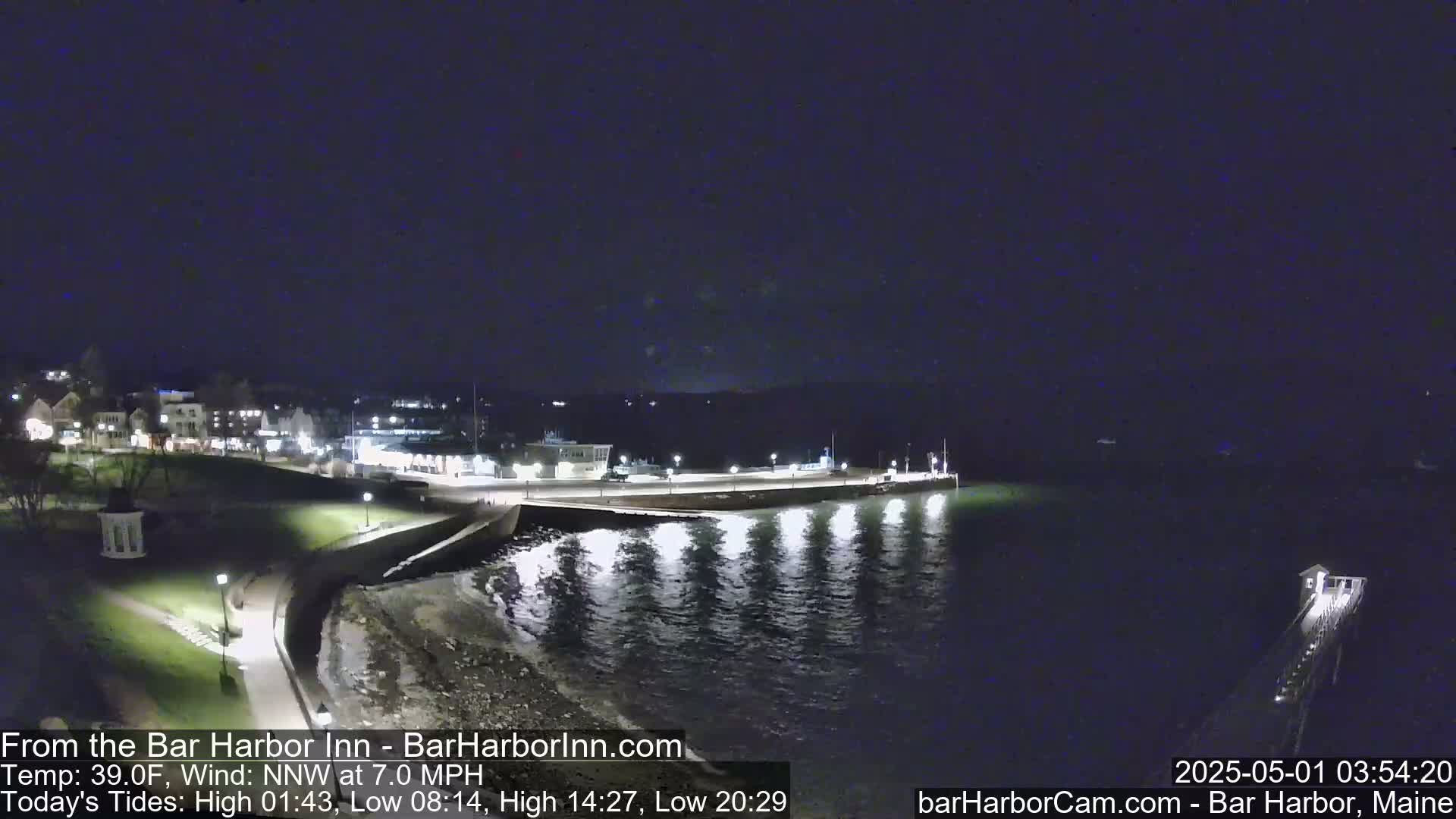 A nighttime view of a calm harbor with a town's lights in the background, under a dark sky.