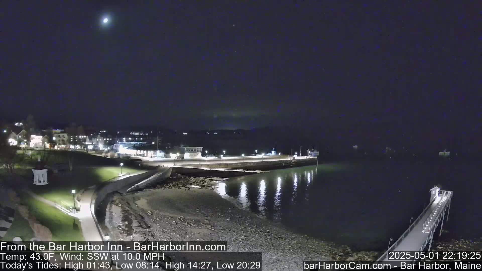 A nighttime coastal scene shows a calm harbor with a pier extending into the water, under a clear, dark sky with a bright star visible.