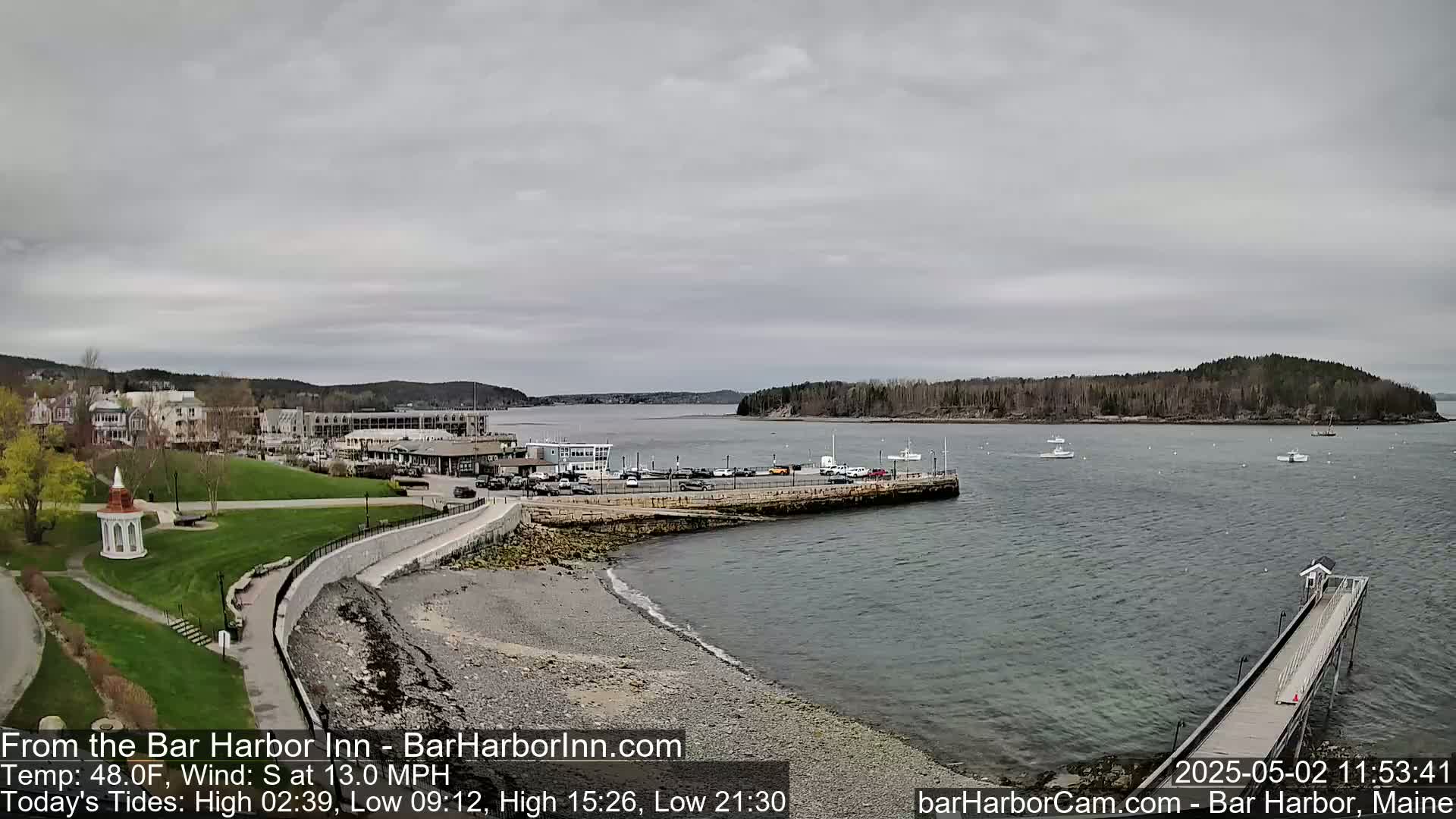 A coastal town with a harbor, a small island, and several boats is viewed on an overcast day with a south wind.