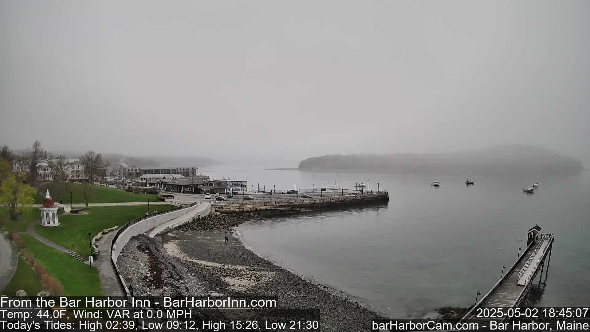 A foggy coastal town scene shows a harbor with a few boats, a long pier, and a stone walkway along a rocky shore.