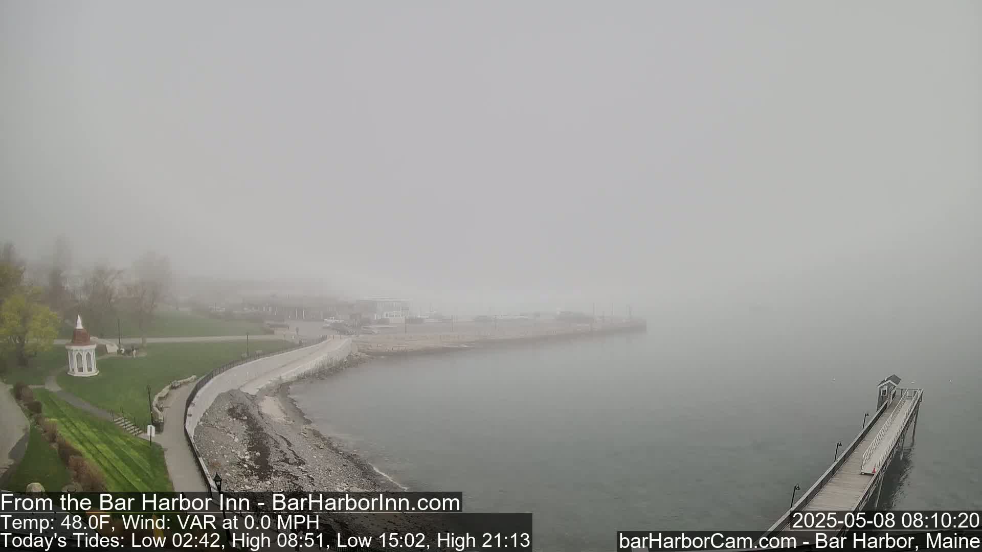 A foggy coastal scene shows a walkway along the water's edge leading to a pier, with a gazebo and park visible in the background.
