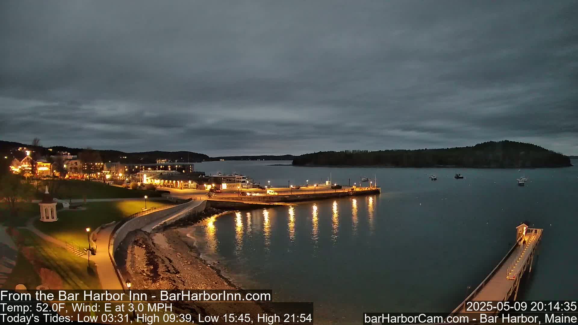 A nighttime view of a harbor town with a calm, dark sky, illuminated buildings along the shore, and several boats in the water.