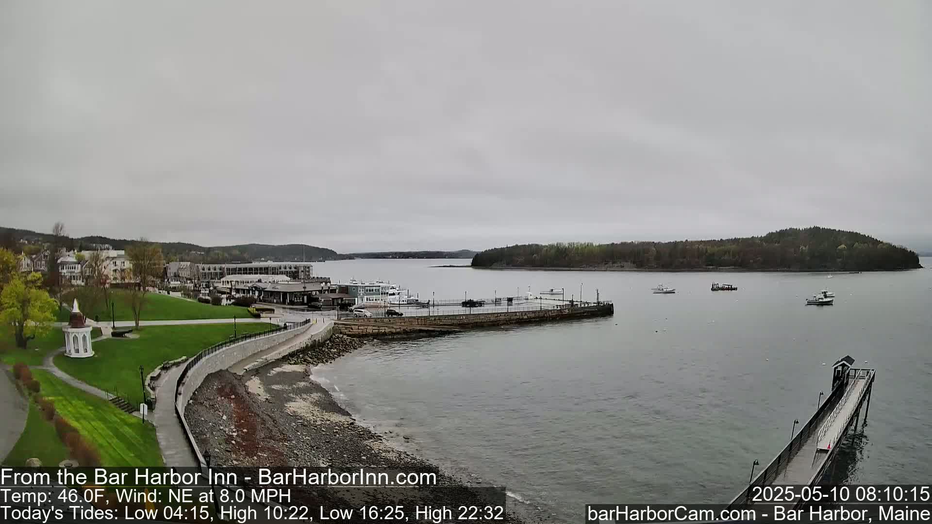 A gray, overcast day reveals a coastal town with a harbor, a grassy park, and several boats, all viewed from an elevated perspective.