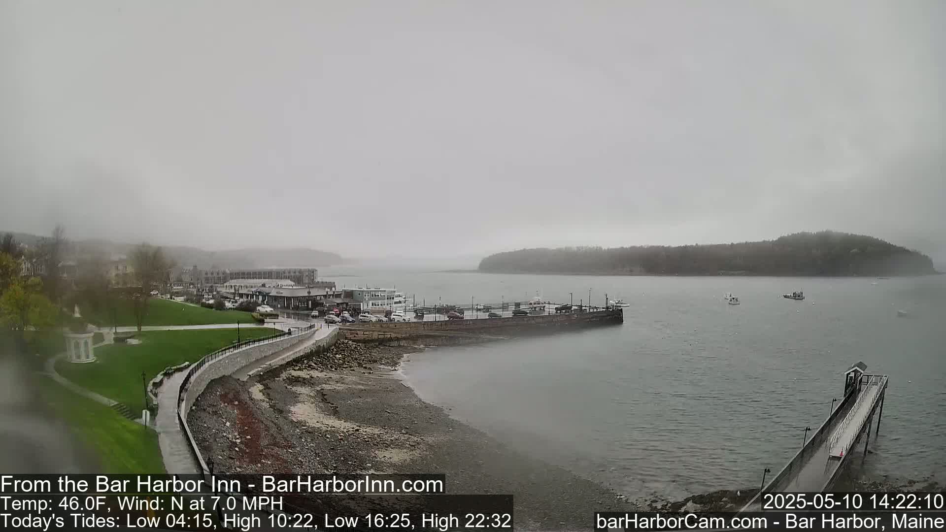 A foggy coastal town scene shows a harbor with boats, a long pier, and buildings along the shoreline, with a grassy park area.