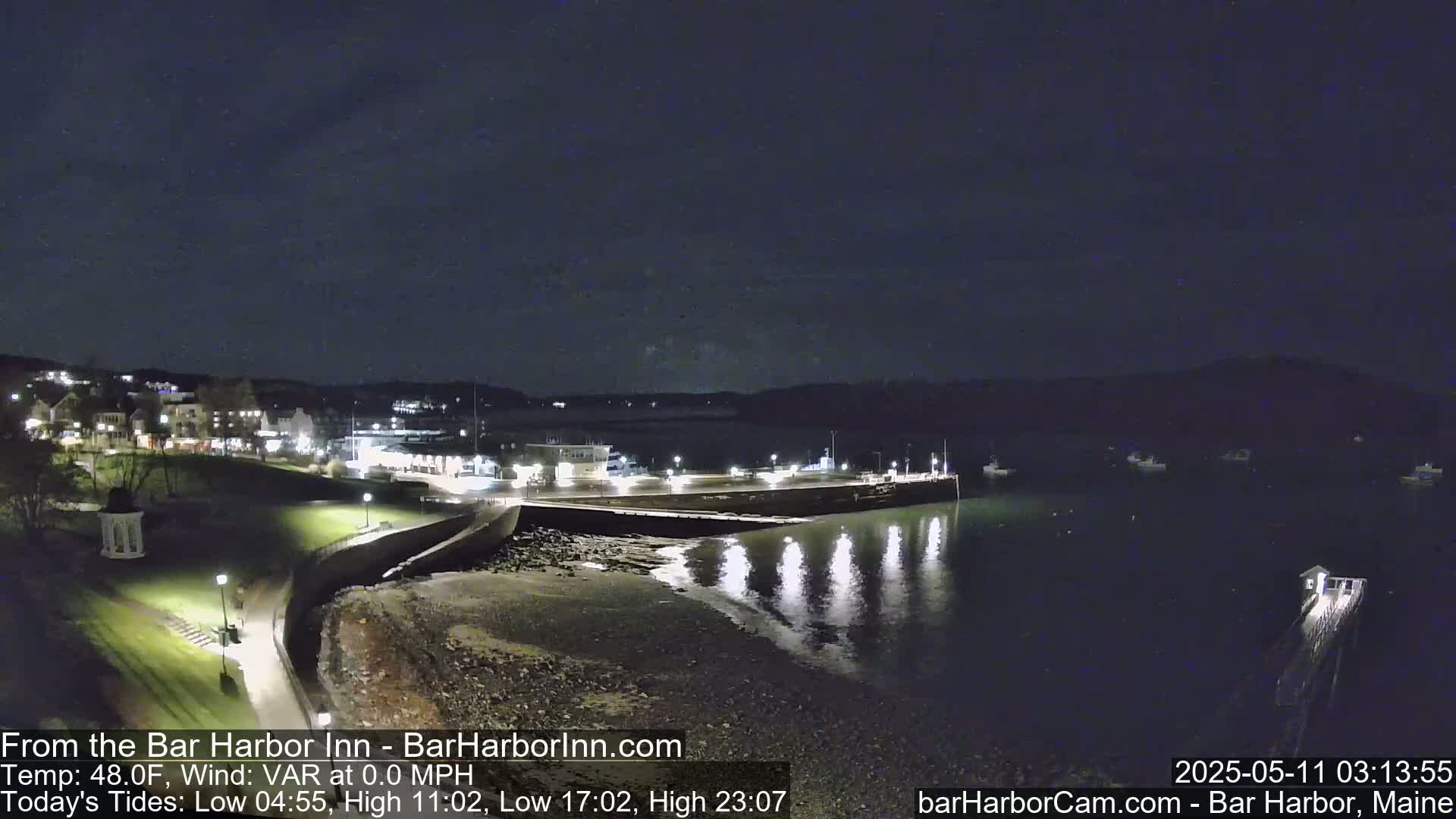 A nighttime view of a calm harbor with a town's lights visible in the background, under a dark sky.
