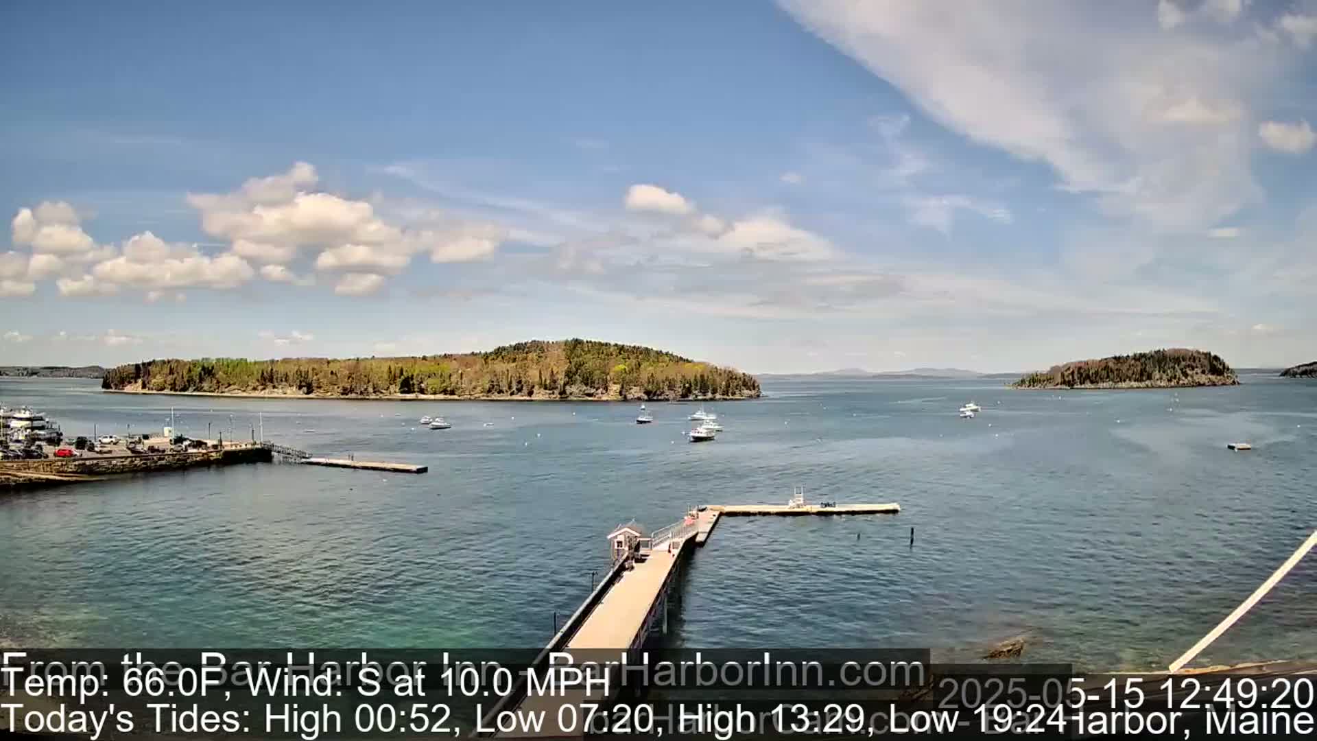 A calm, sunny day reveals a harbor with several boats, a long pier, and a small, tree-covered island in the distance.