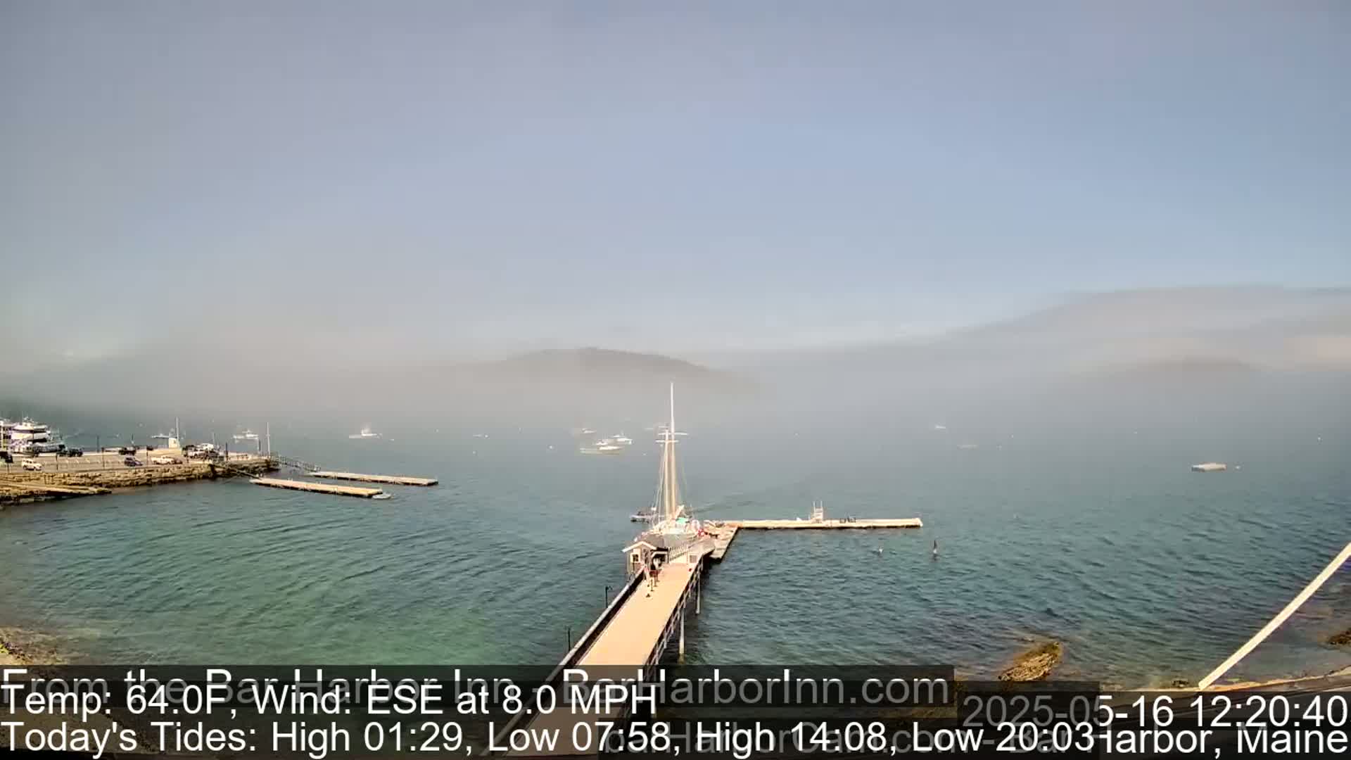 A hazy harbor scene shows a long pier extending from a rocky shore into calm water, with several boats and docks visible in the distance.