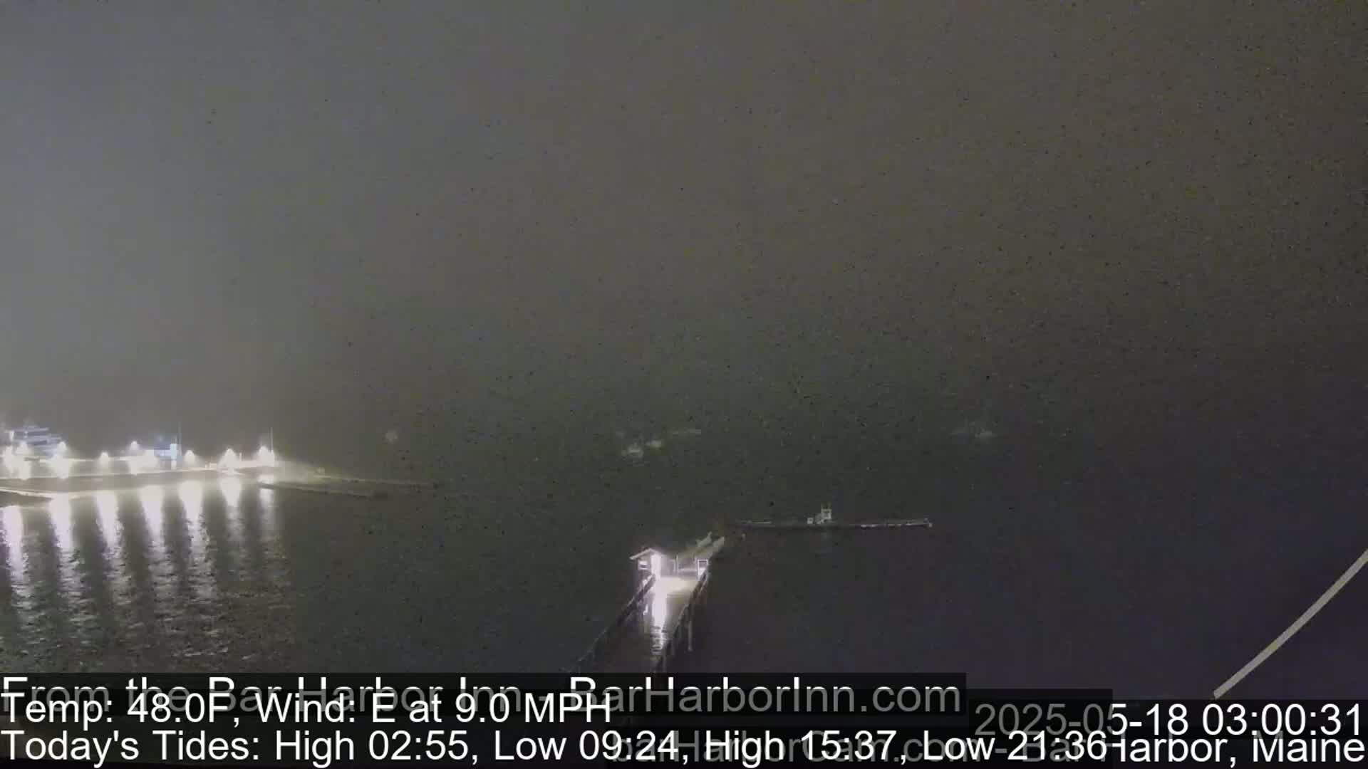 A nighttime harbor scene shows a pier extending into dark, choppy water under a foggy sky with an easterly wind.