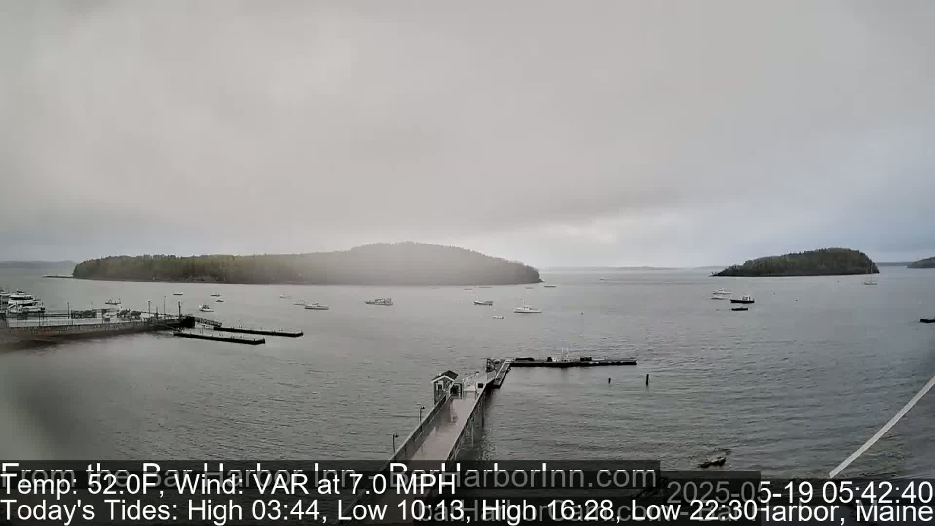 A harbor scene on an overcast day shows several boats moored near a long pier extending into the water, with islands visible in the distance.