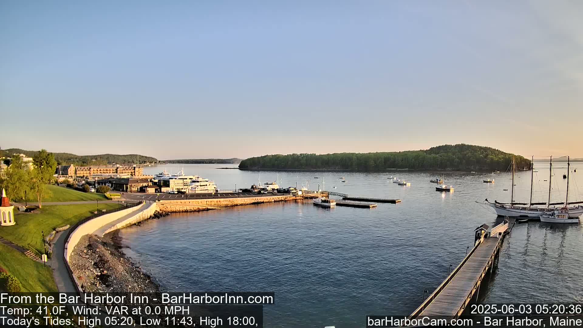 A calm harbor with numerous boats and a large hotel is seen from an elevated vantage point on a clear, cool morning.