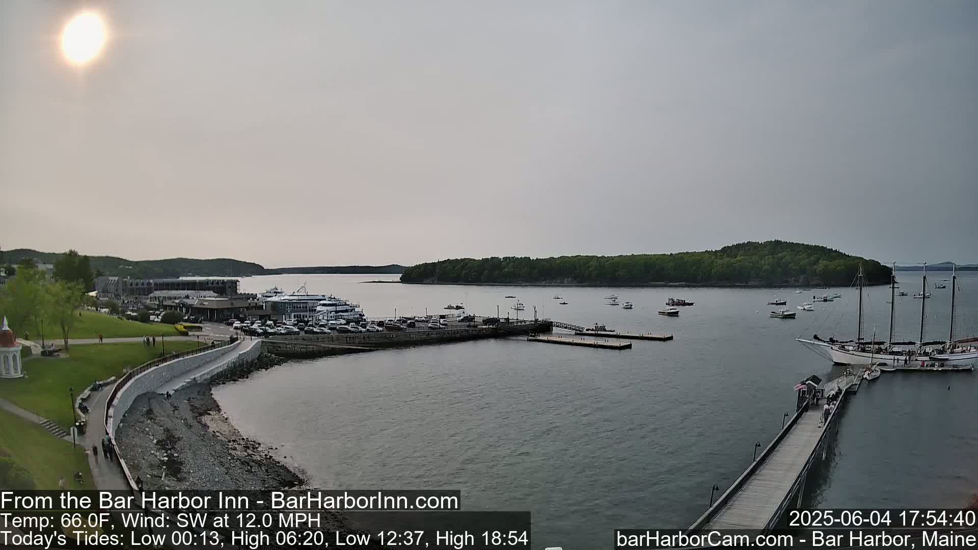 A harbor scene on a partly sunny day with a southwest wind shows a waterfront with docked boats, a large sailing ship, and a small island in the distance.