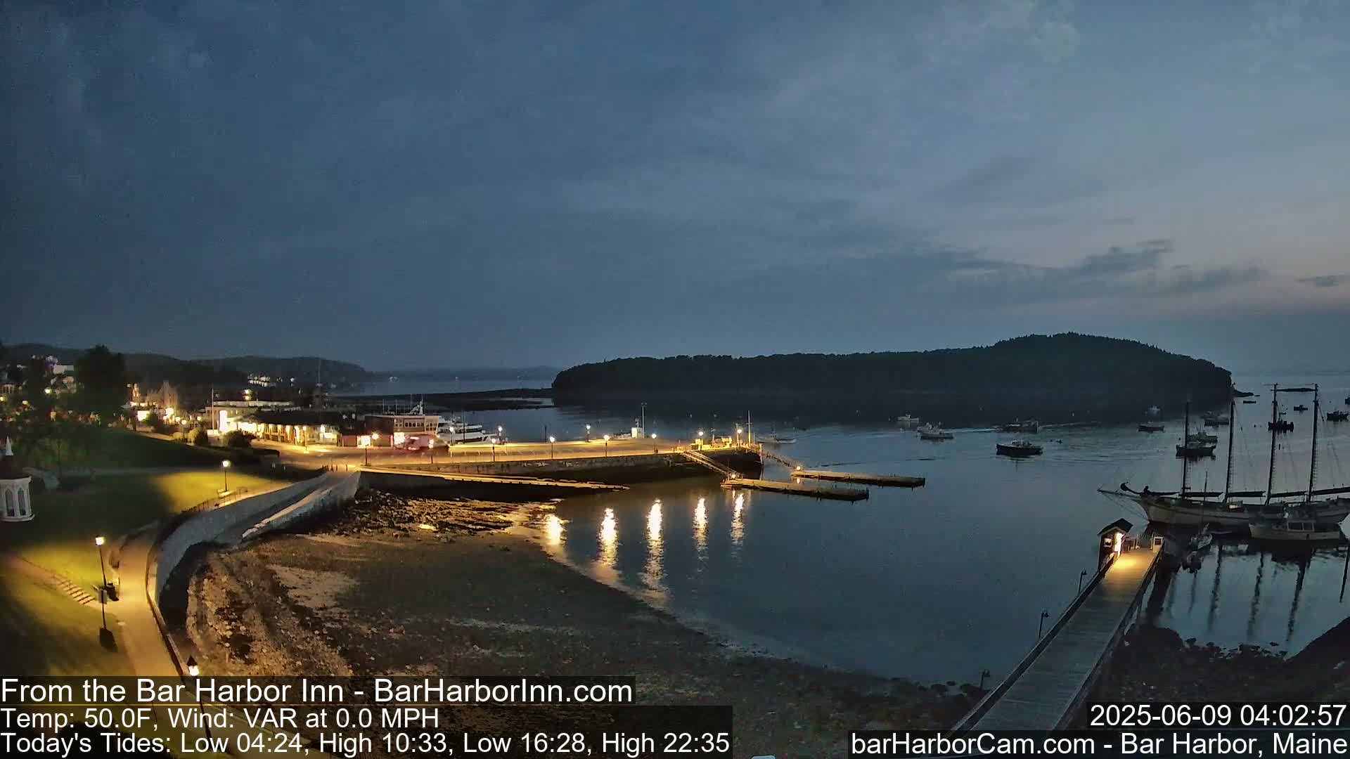 A nighttime view of a harbor with boats and a town illuminated under a partly cloudy sky.