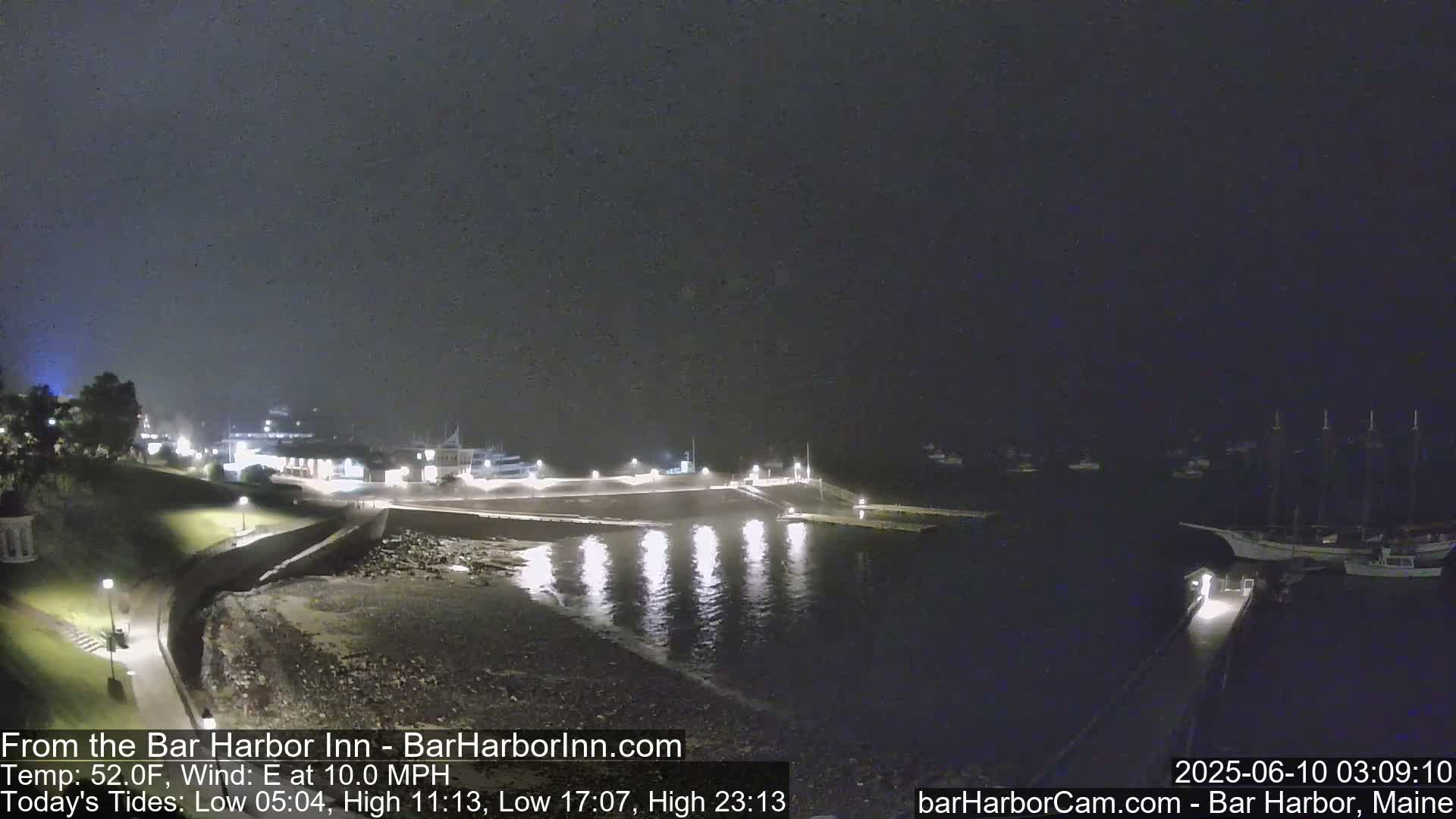 A nighttime view of a harbor with boats and a shoreline, under a dark, overcast sky.